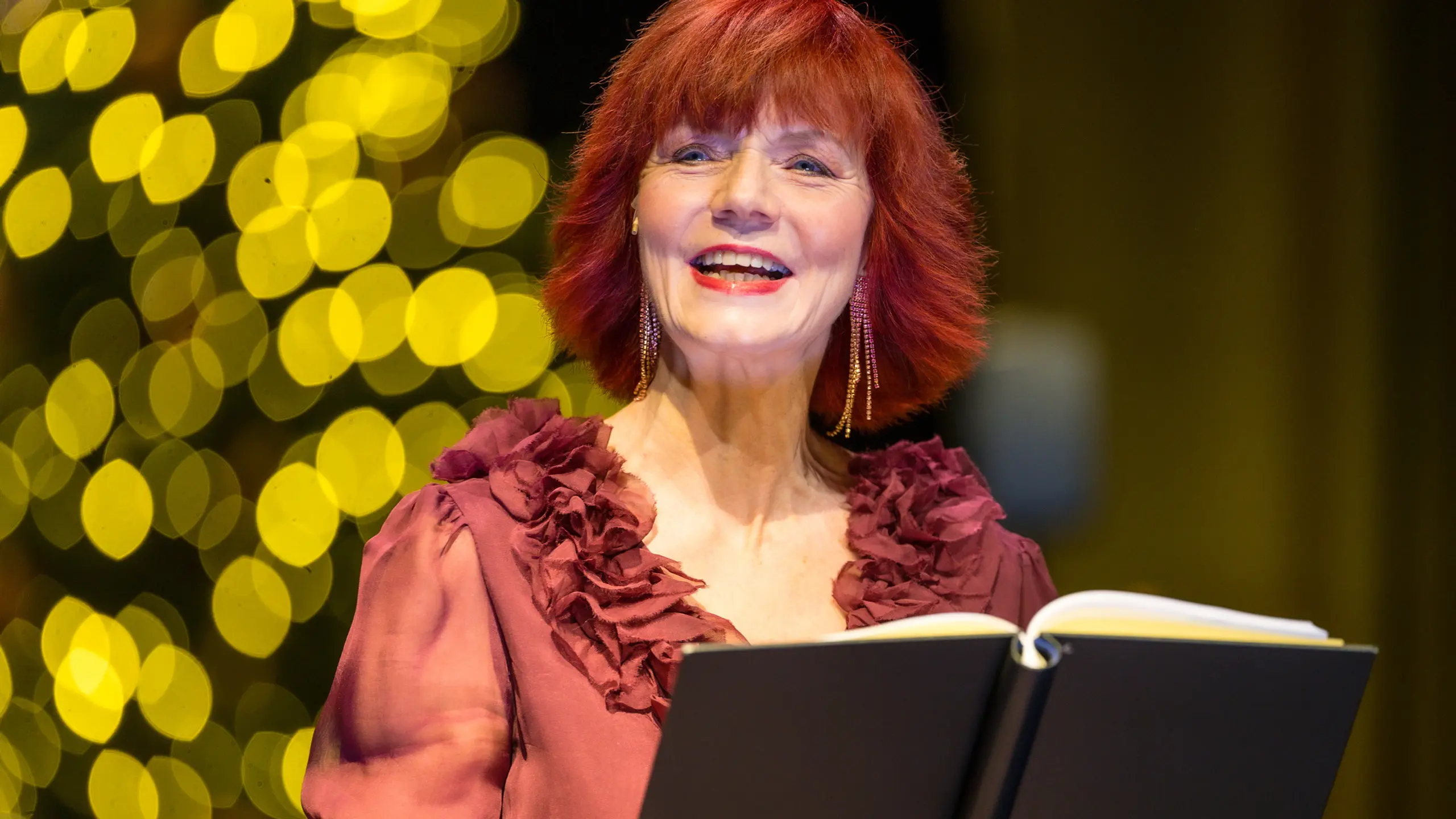 Smilende kvinne med fine klær som holder en bok foran seg