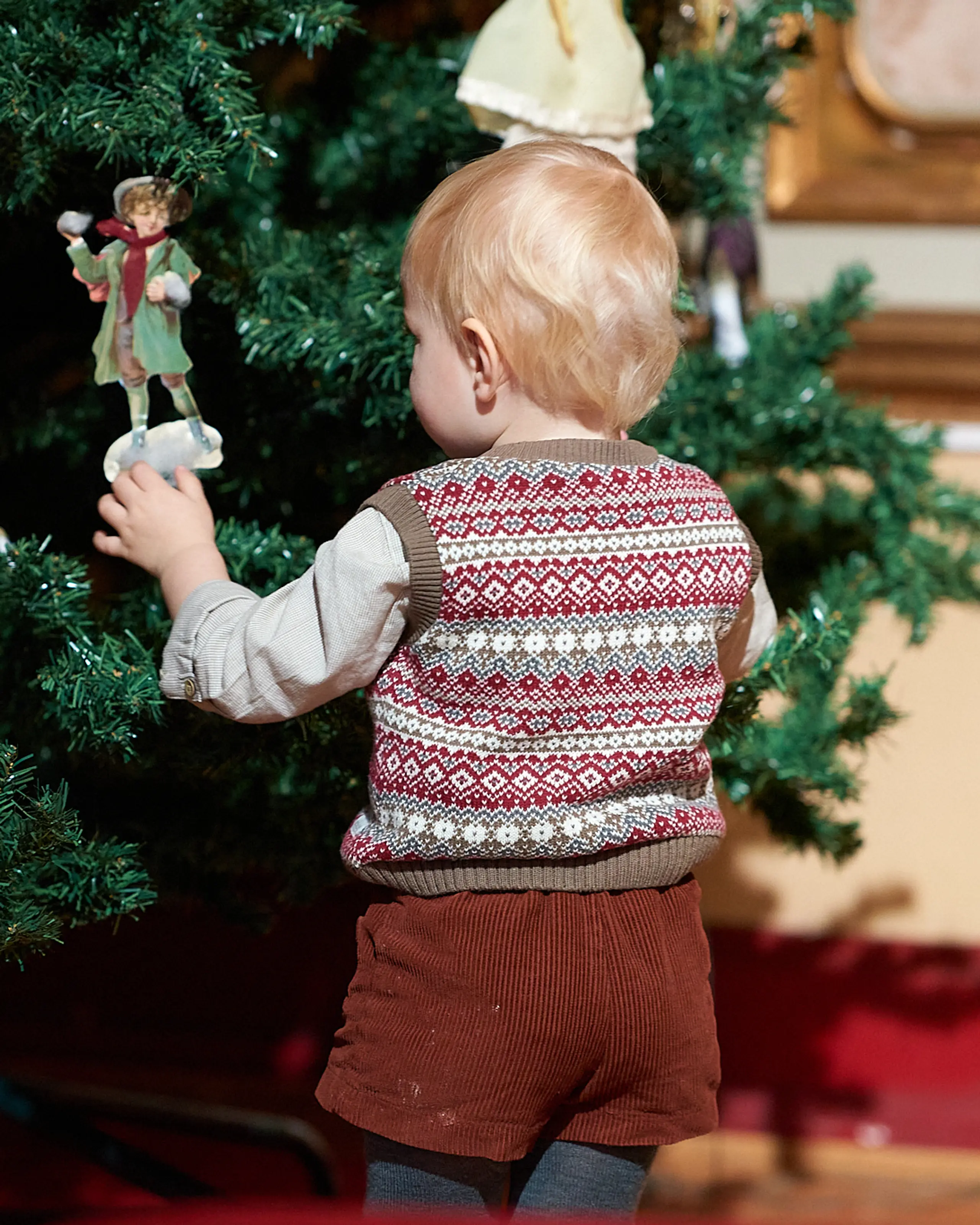 En liten gutt står og holder på en engel som henger på et juletre
