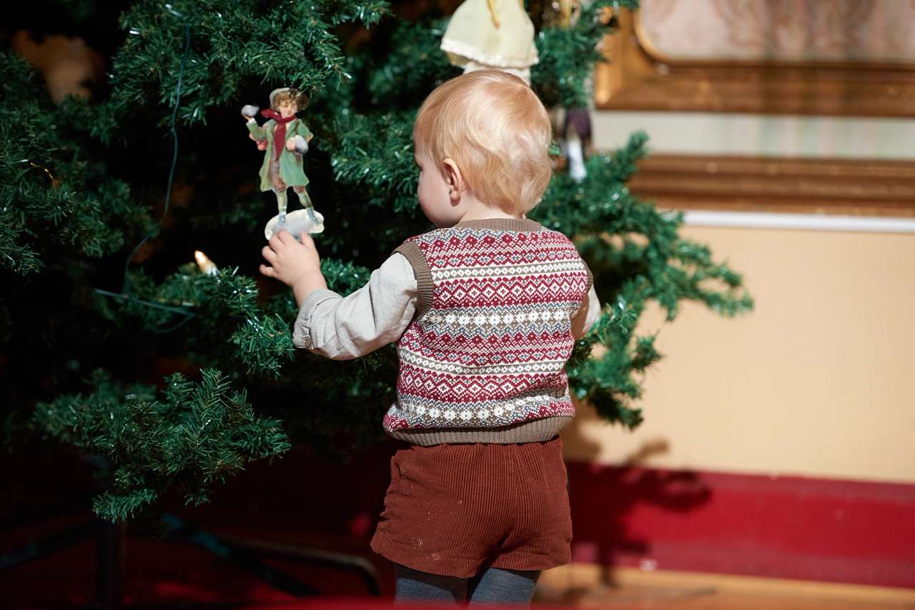 En liten gutt står og holder på en engel som henger på et juletre