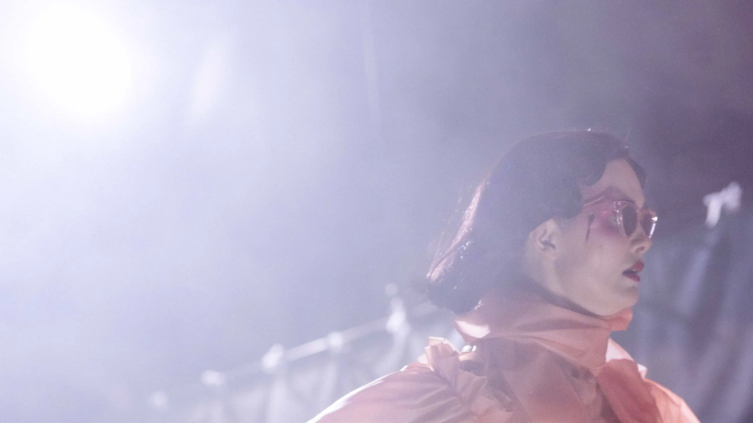 Person i ferskenfarget kjole og solbriller går over scenen mens hun holder en pistol i hånden