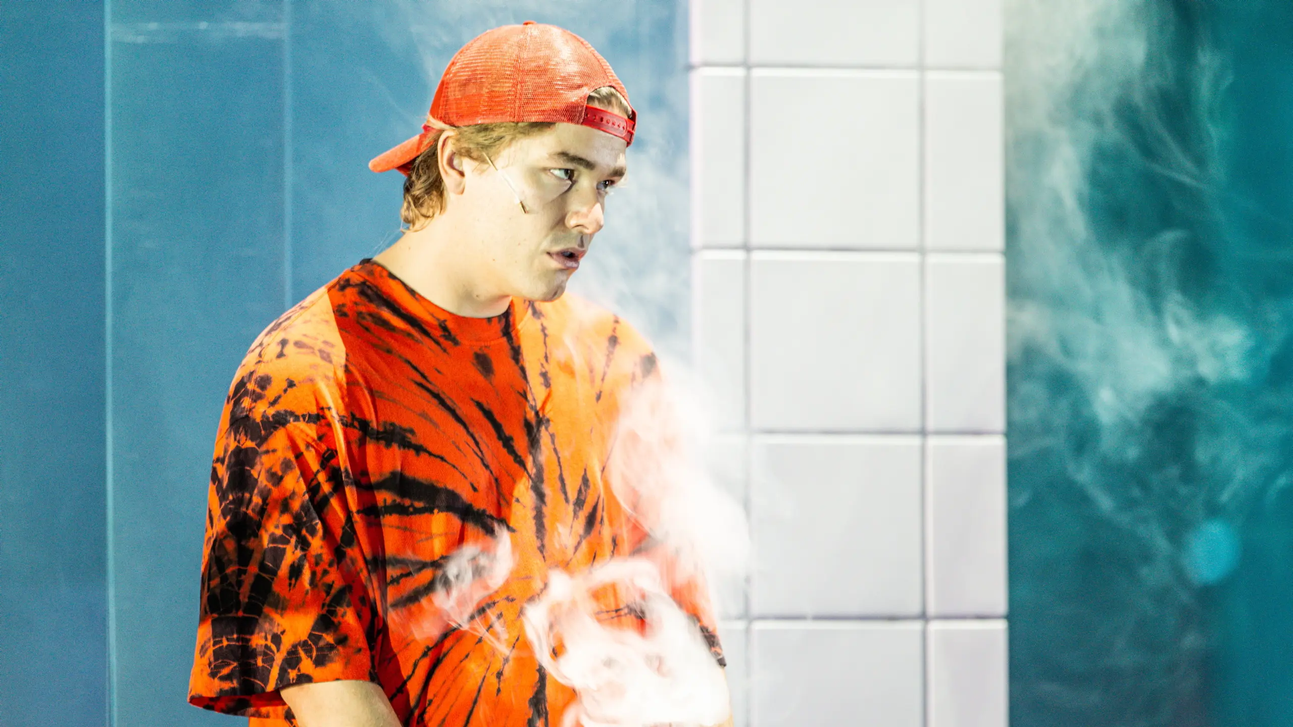 Mann med oransje caps bak fram i røyk