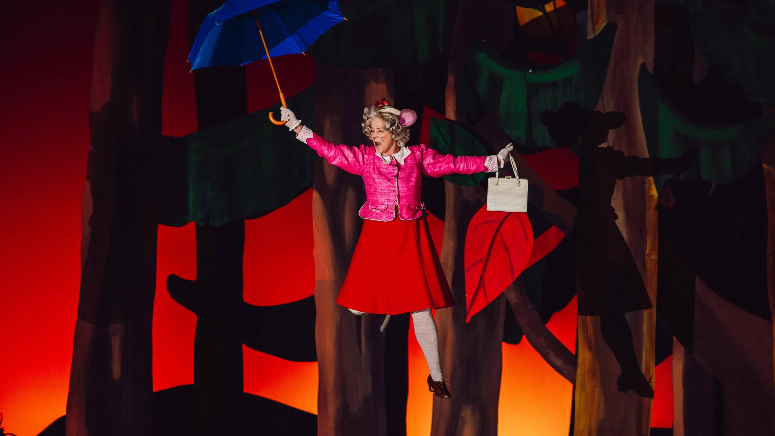 En karakter i rosa jakke og rød skjørt henger i luften med blå paraply og hvit veske foran malt skogsbakgrunn.