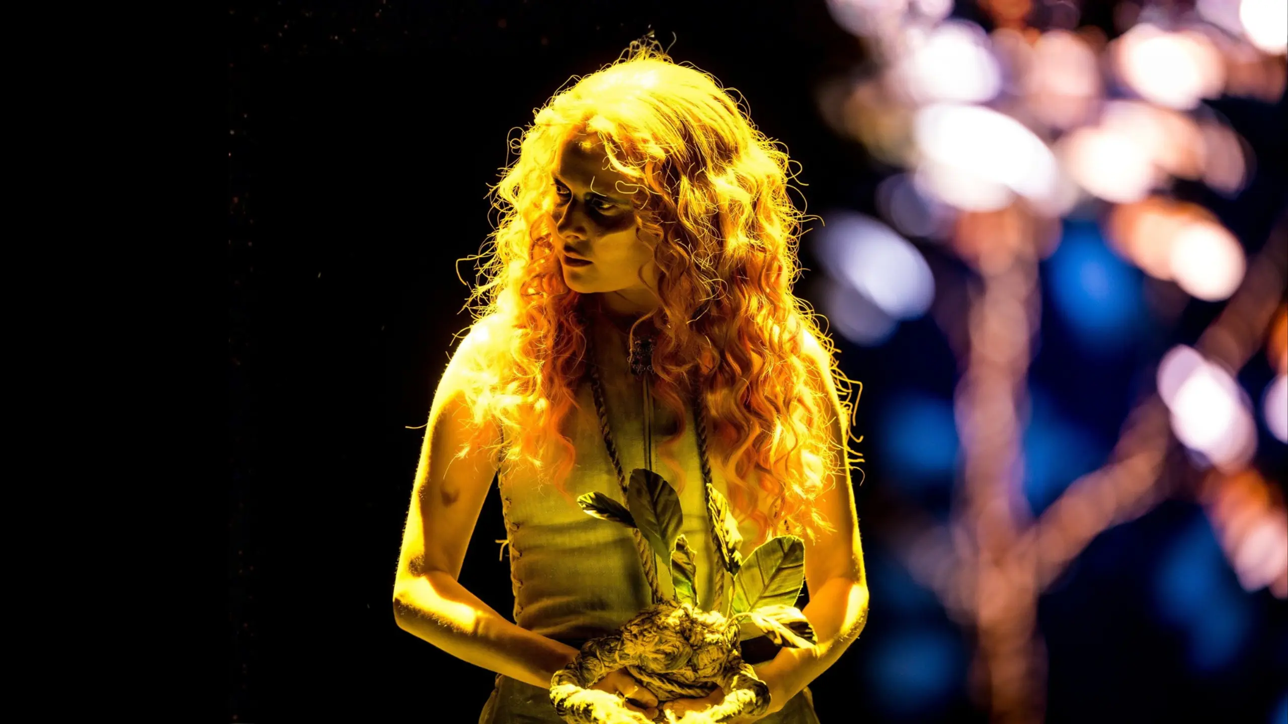 Kvinne med gult lys på seg, mens hun holder en rotlignende figur