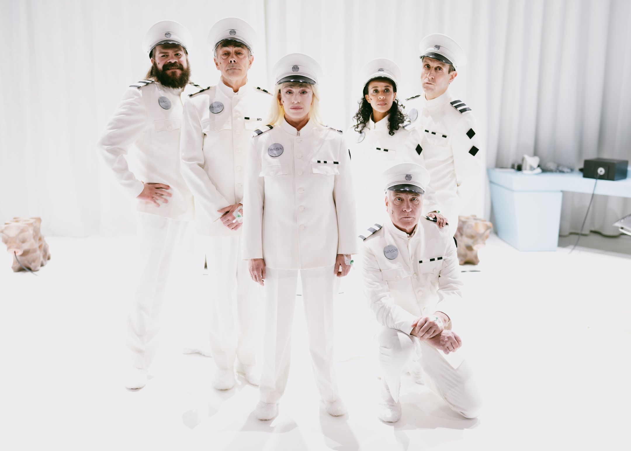 Seks personer i hvite futuristiske kostymer stilt opp til gruppebilde