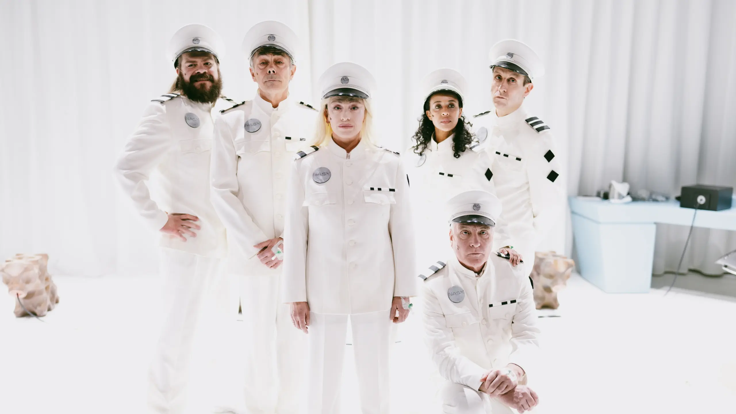Seks personer i hvite futuristiske kostymer stilt opp til gruppebilde