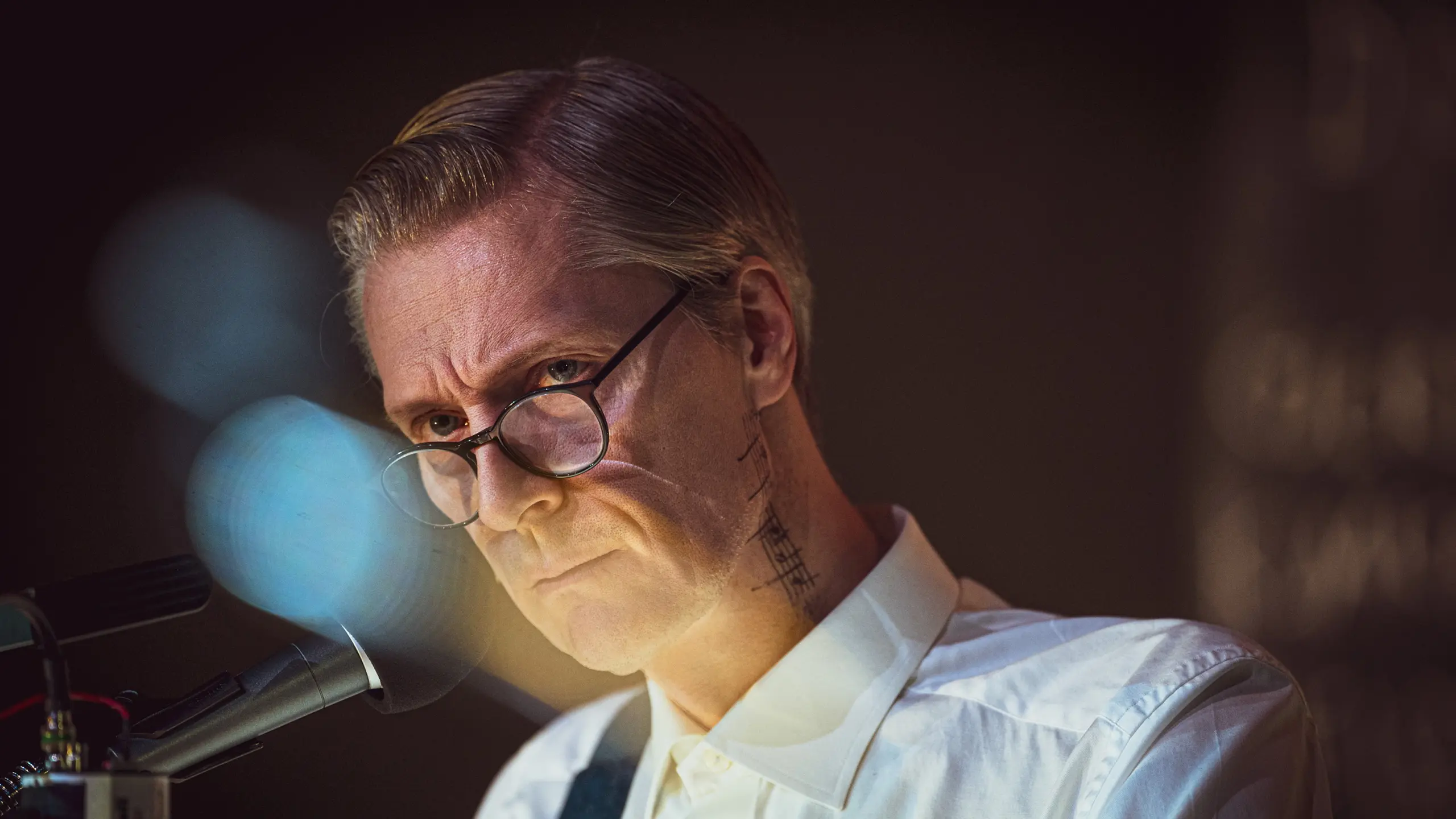 Mann med briller og noter på halsen snakker i mikrofon