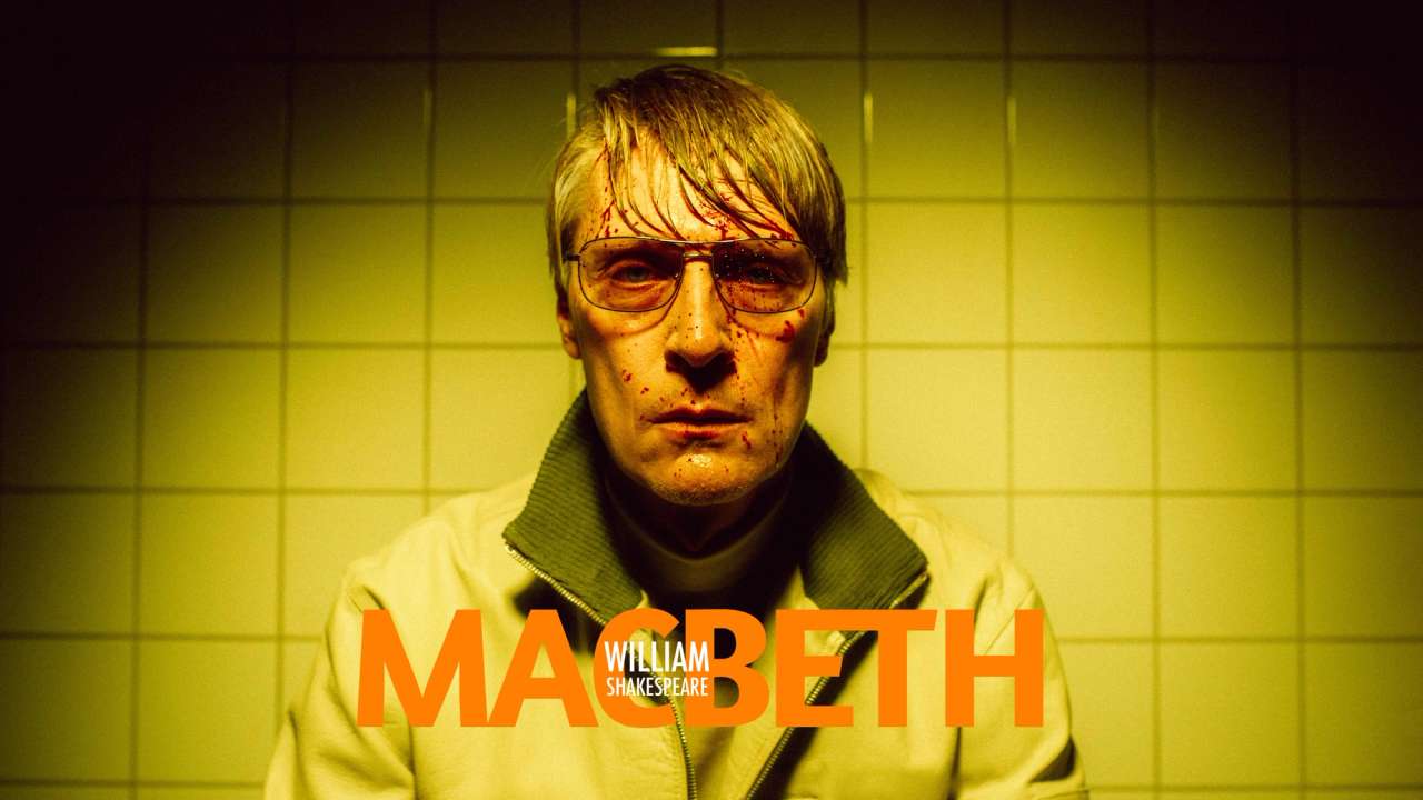 Svett mann med solbriller og blodsprut i fjeset i gult lys. Hvite fliser på veggen bak med tittel "Macbeth William Shakespeare"