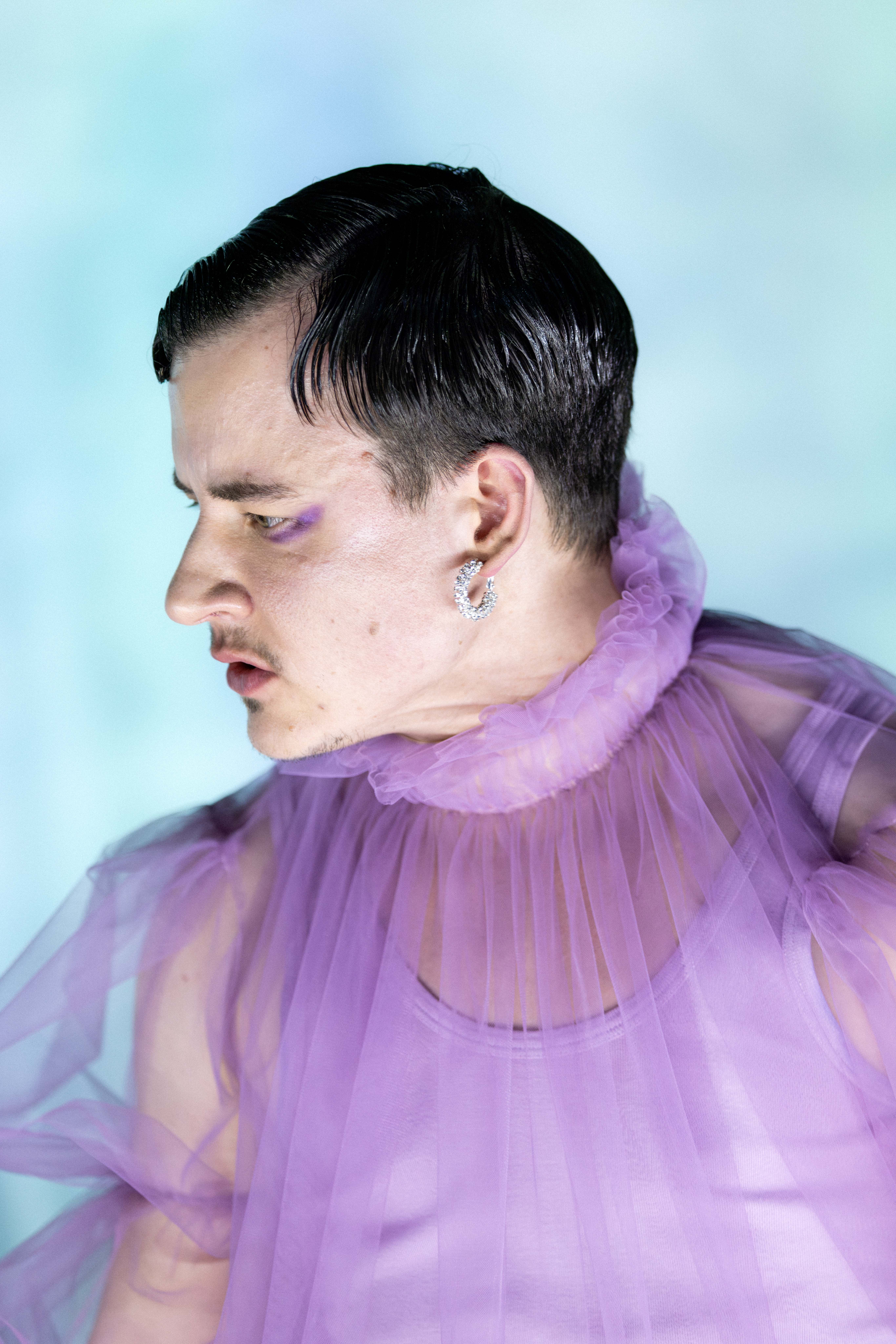 Nærbilde av person i lilla tyllkostyme med kort hår og øredobb, ser til siden