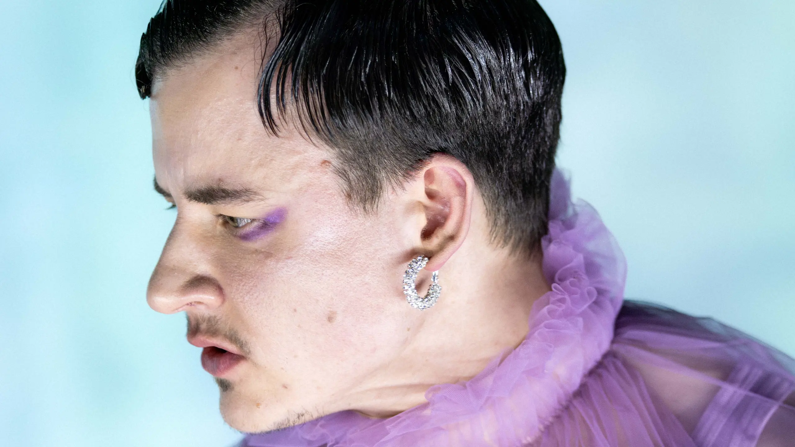 Nærbilde av person i lilla tyllkostyme med kort hår og øredobb, ser til siden