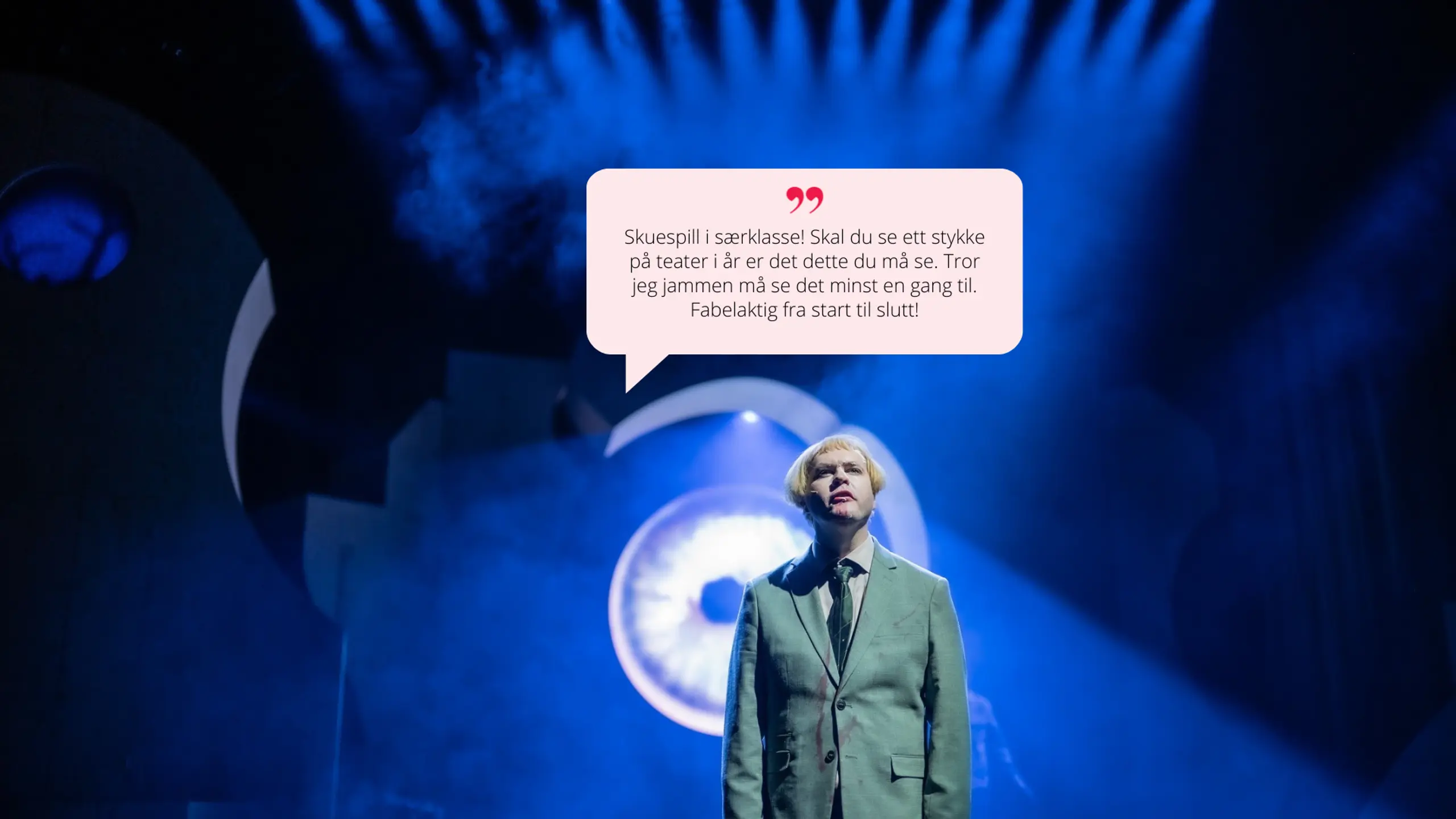 En skuespiller i lysegrønn dress står under et blått scenelys med en enorm, lysende projeksjon av et øye i bakgrunnen. Det skapes en dramatisk og intens stemning. Sitat i snakkeboble: "Skuespill i særklasse! [...] Fabelaktig fra start til slutt!"