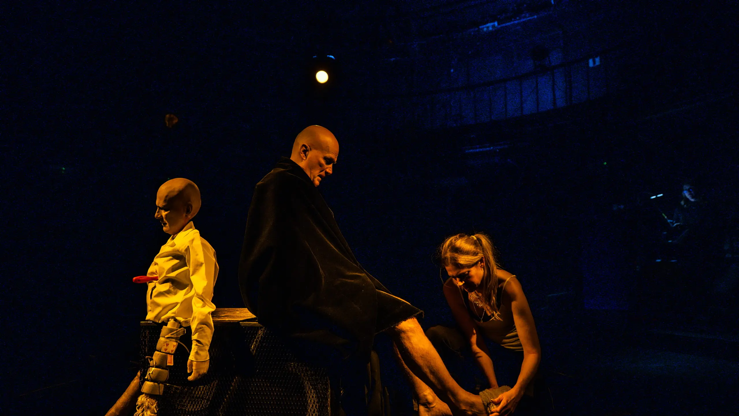 Kvinne bøyer seg ned og bandasjerer mannens bein på scenen, dukke i bakgrunnen