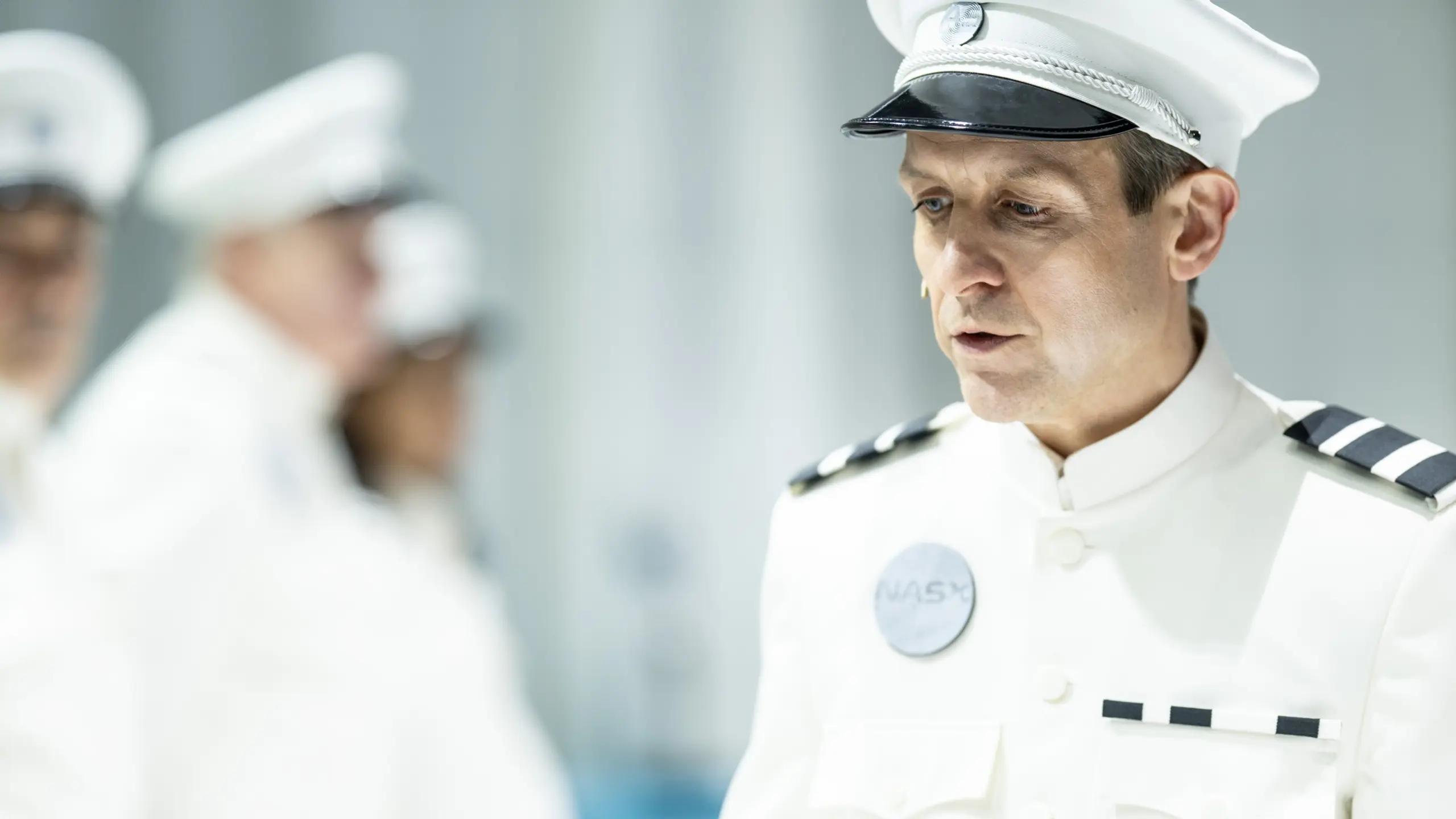 Person i hvit uniform og kaps med merke “NASY”, snakker mens andre uniformerte personer er uklare i bakgrunnen