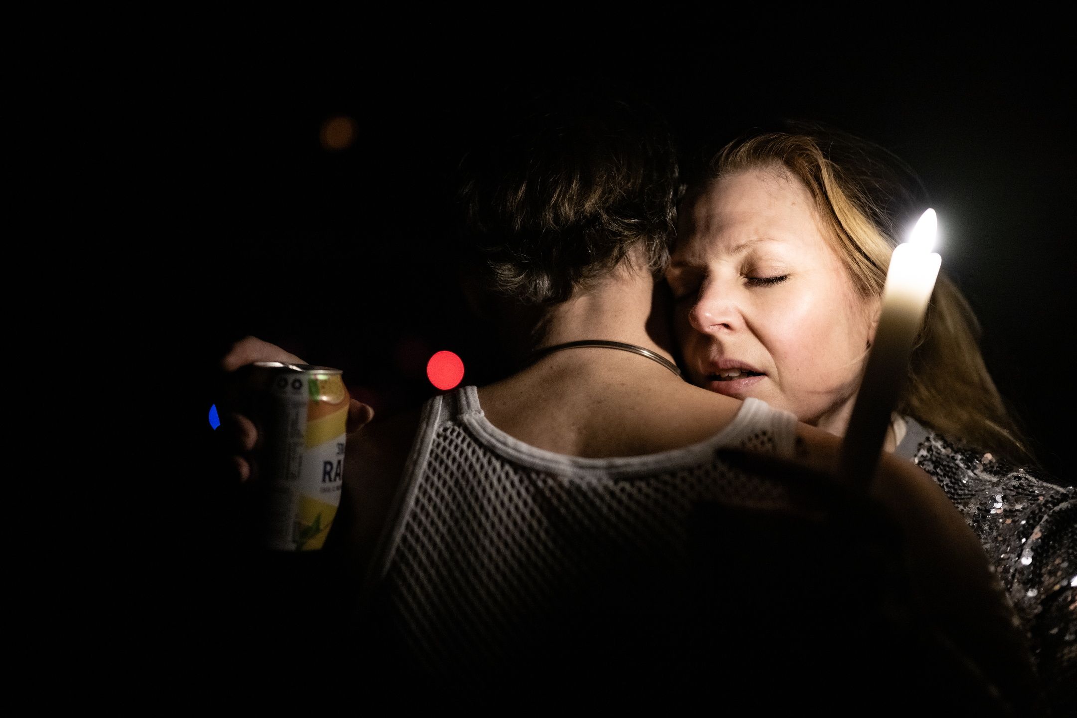 To personer danser tett med lukkede øyne, kvinnen holder et tent lys og den andre en ølboks