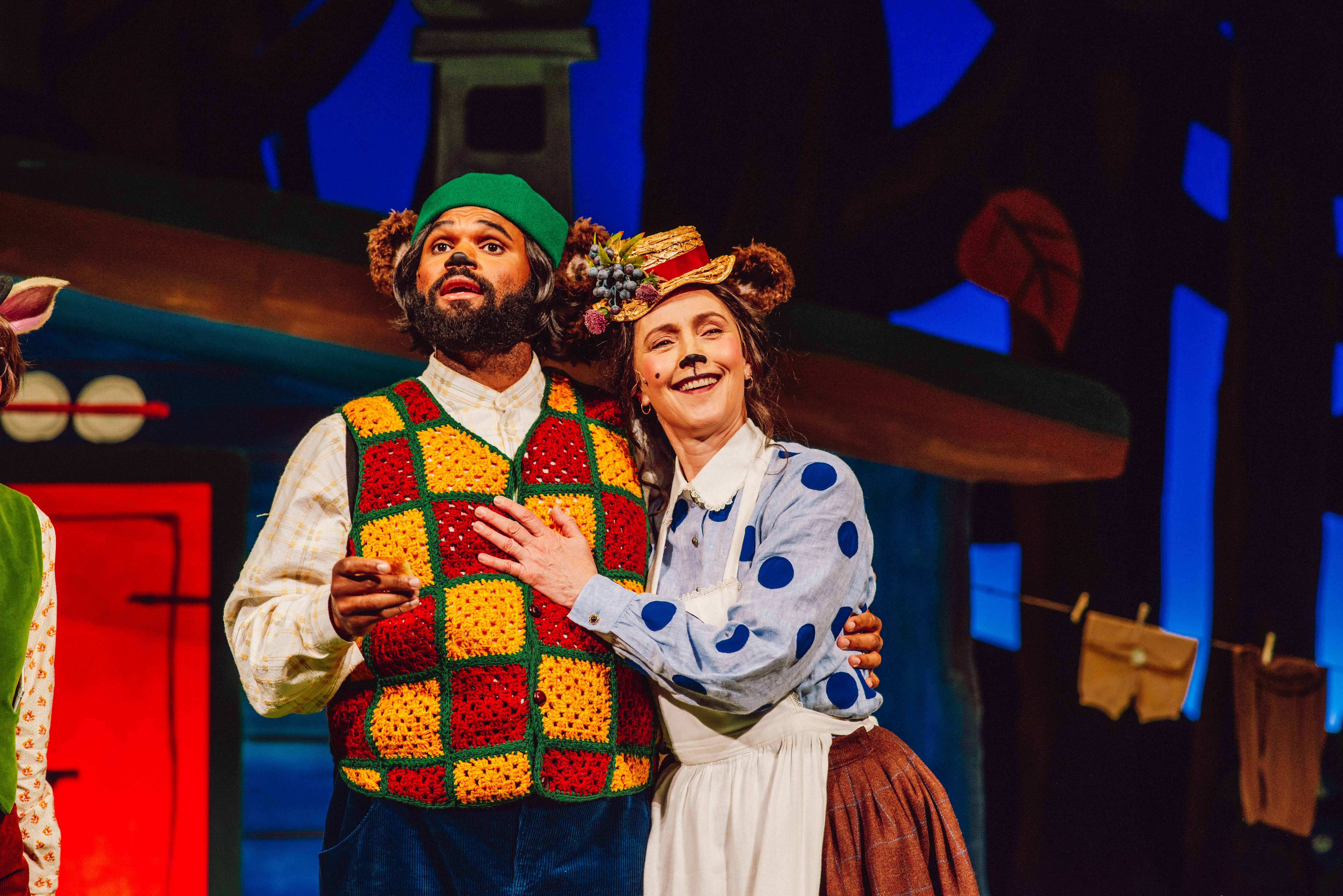 To personer utkledd som bjørner står tett sammen, den ene med fargerik heklet vest og den andre med blå prikkete bluse og blomsterhatt.