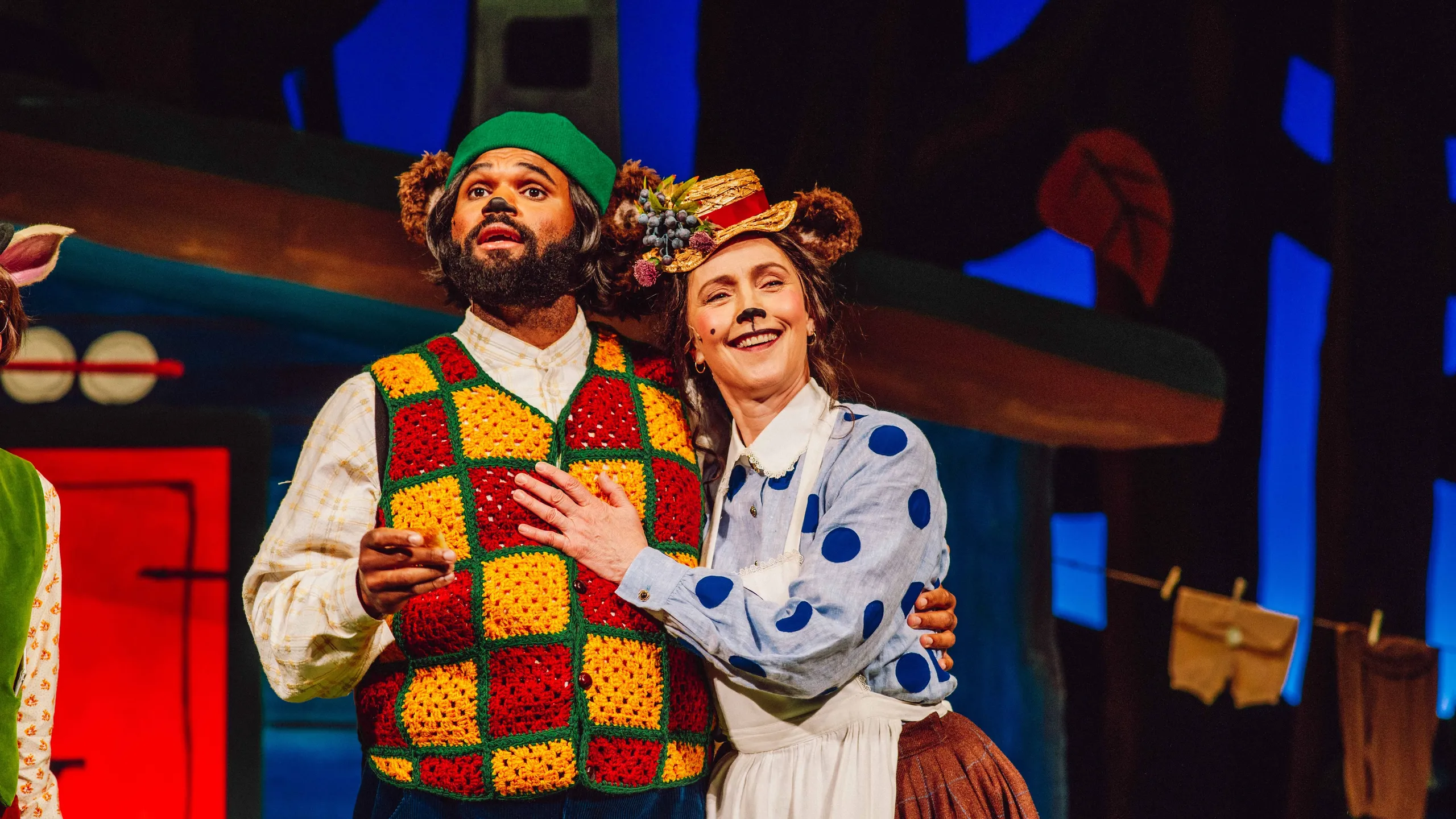 To personer utkledd som bjørner står tett sammen, den ene med fargerik heklet vest og den andre med blå prikkete bluse og blomsterhatt.