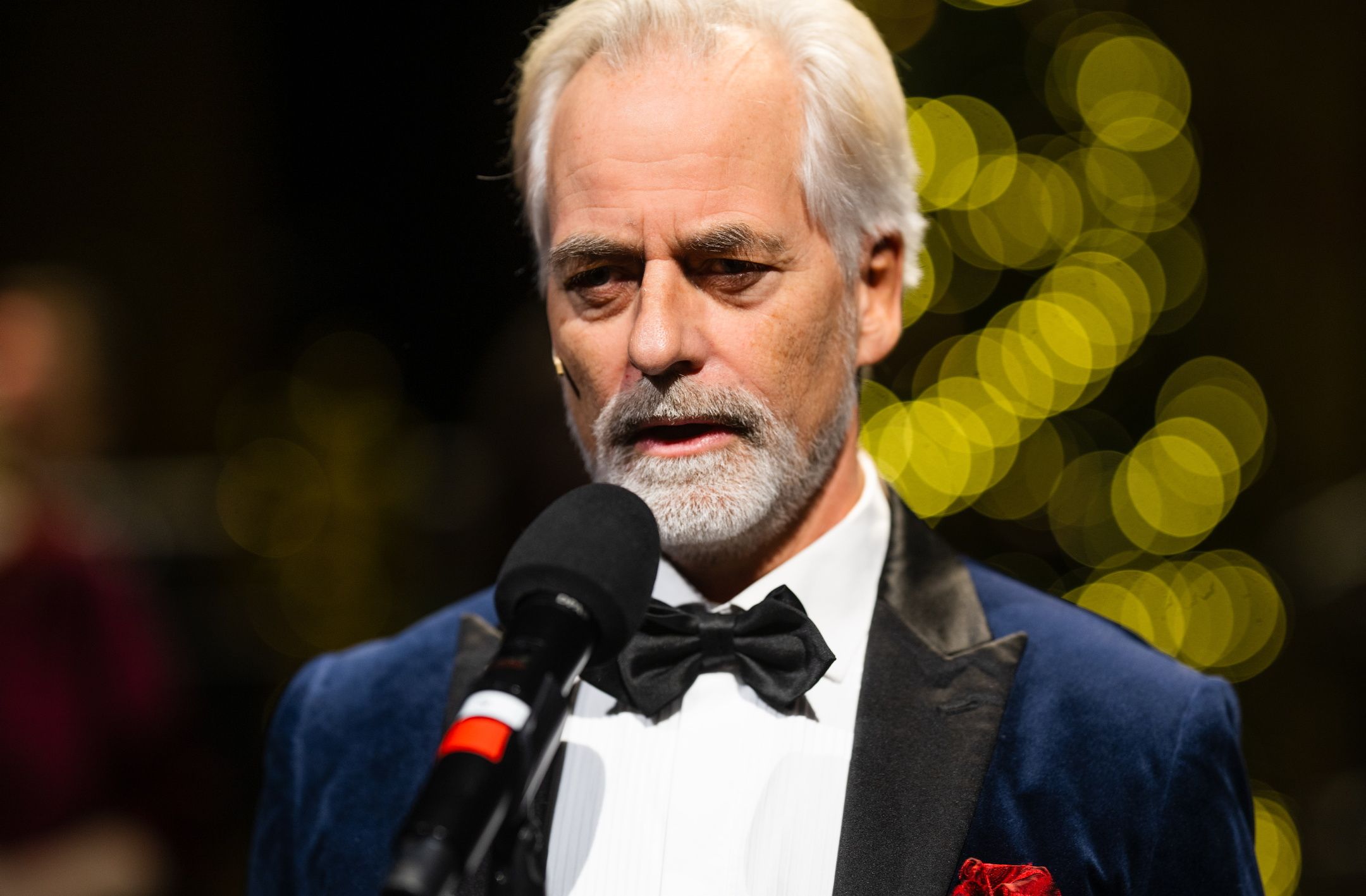 Smokingkledd mann som står foran en mikrofon