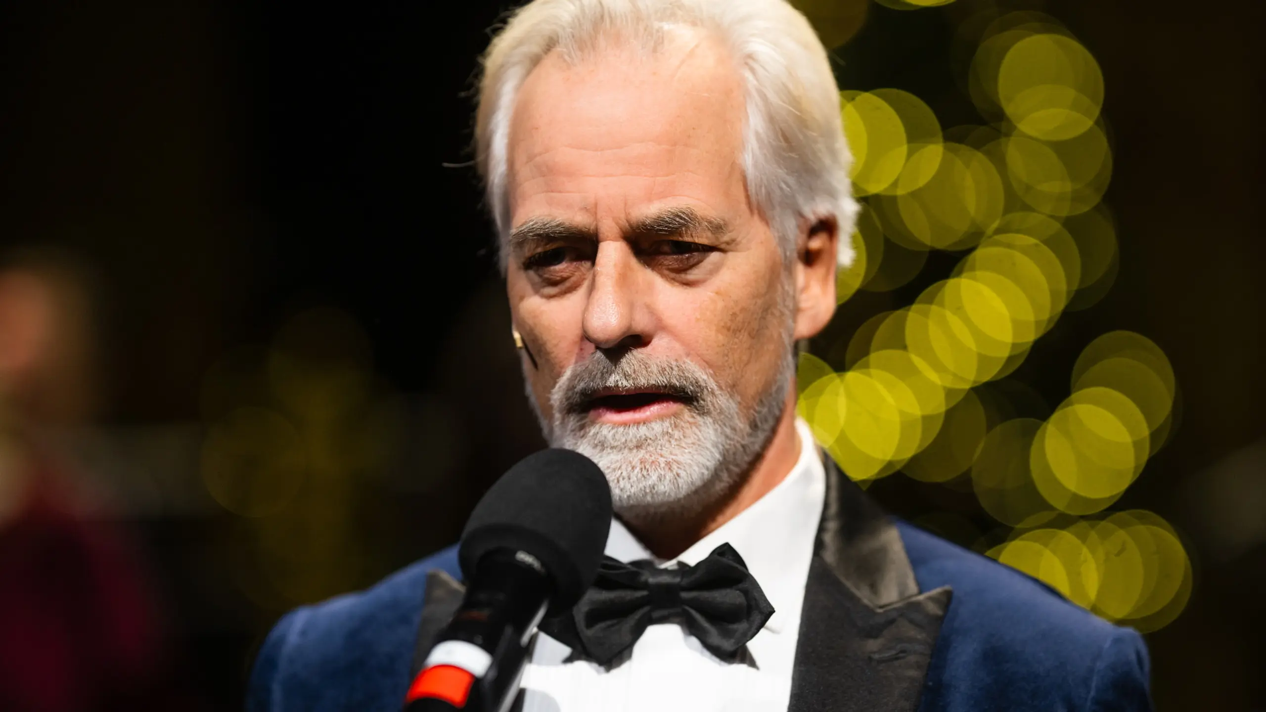 Smokingkledd mann som står foran en mikrofon