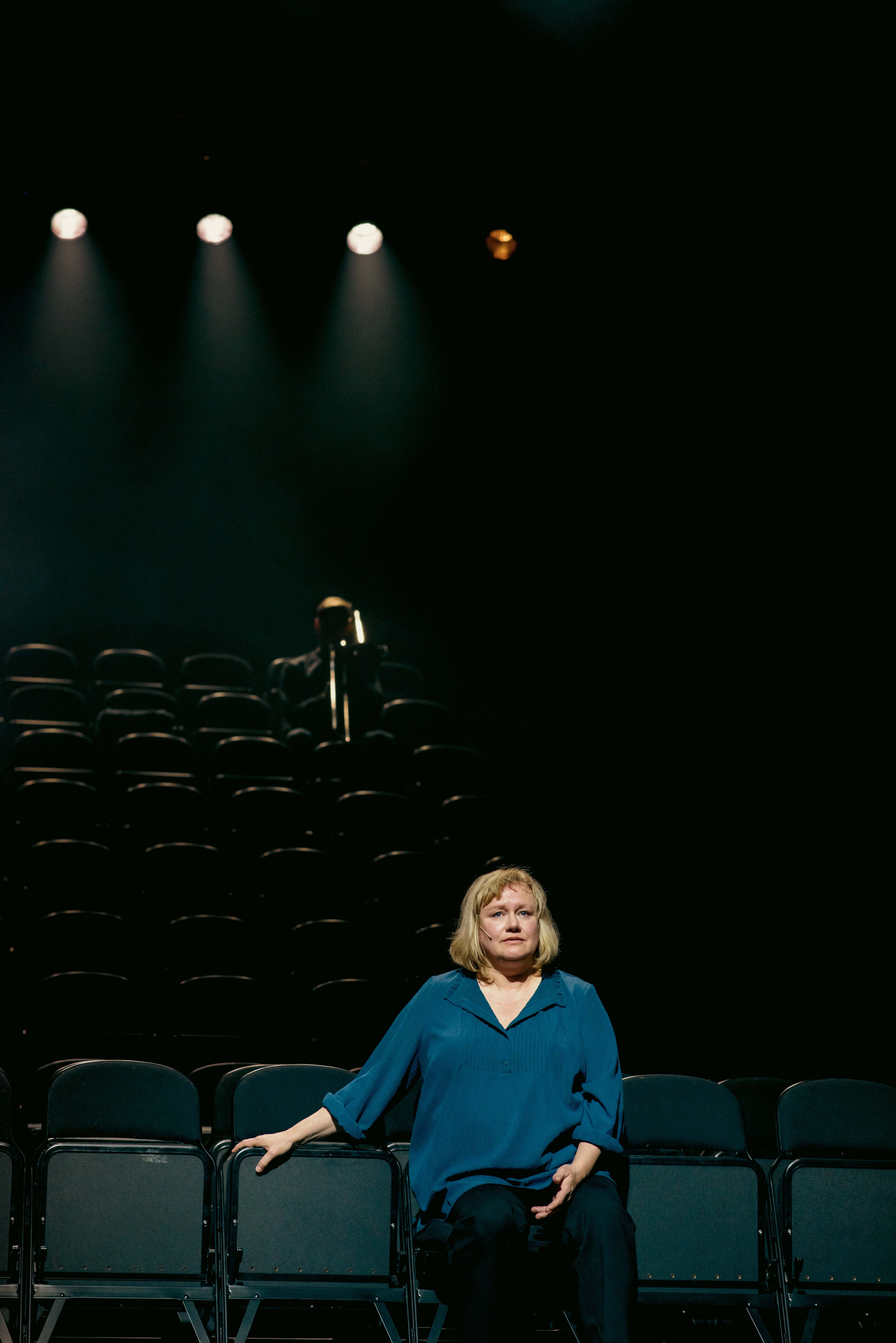 Kvinne sitter fremmerst i et mørkt parti. Bak skimter vi en mann med trombone