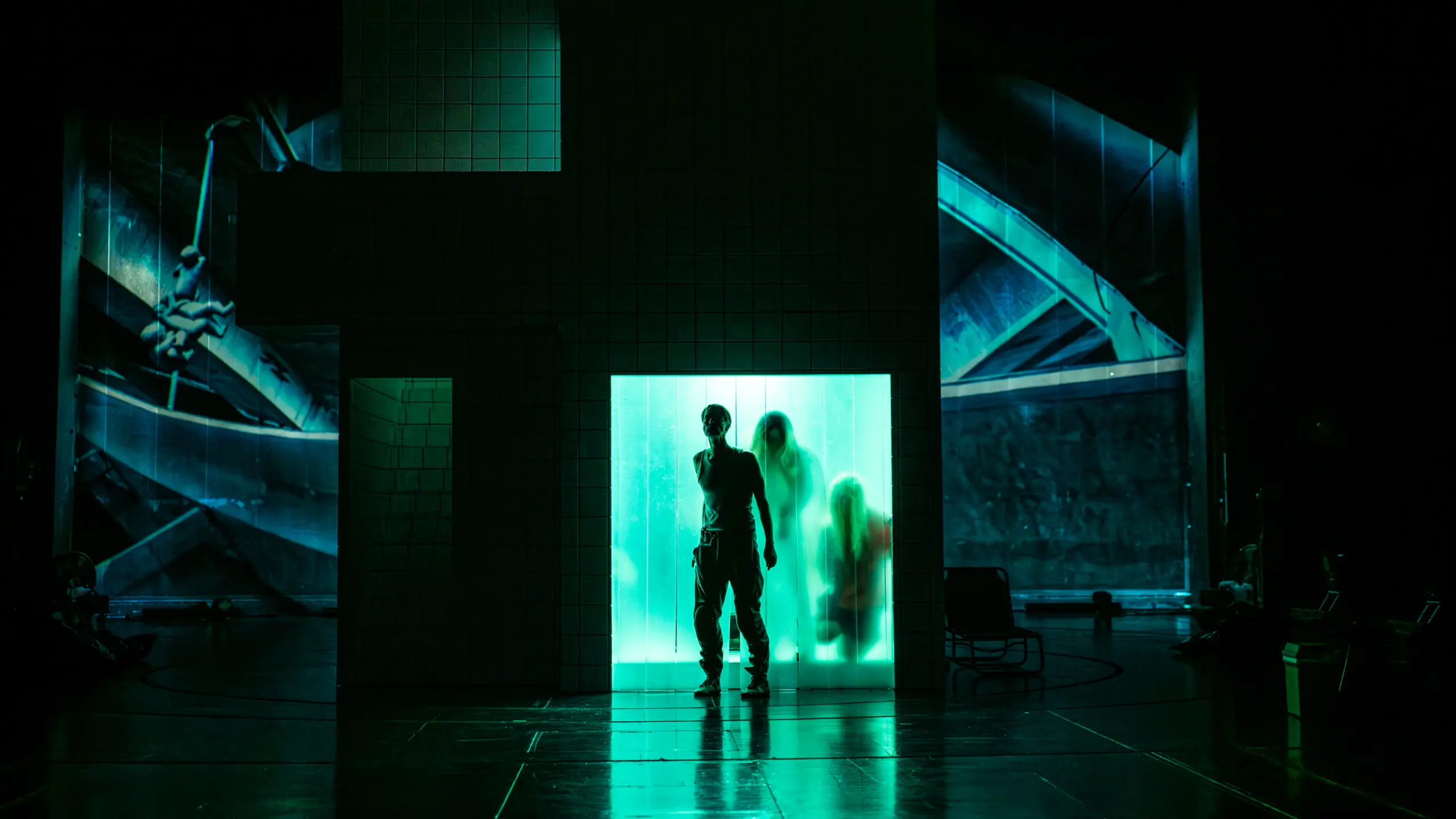 Mørklagt scene med grønn kubeformet struktur, tre skikkelser bak opplyst plastvegg