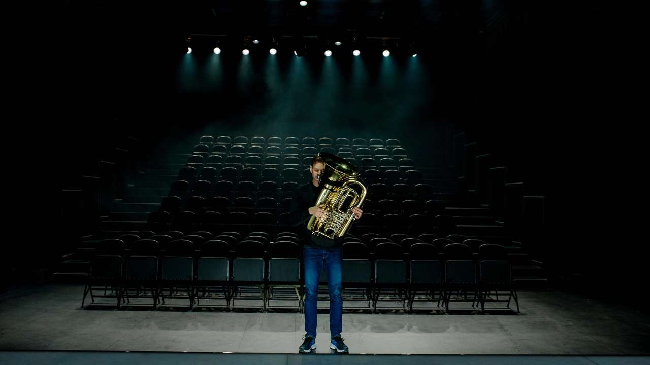 Musiker Kristoffer Kompen står foran et mørkt og tomt amfi med en tuba