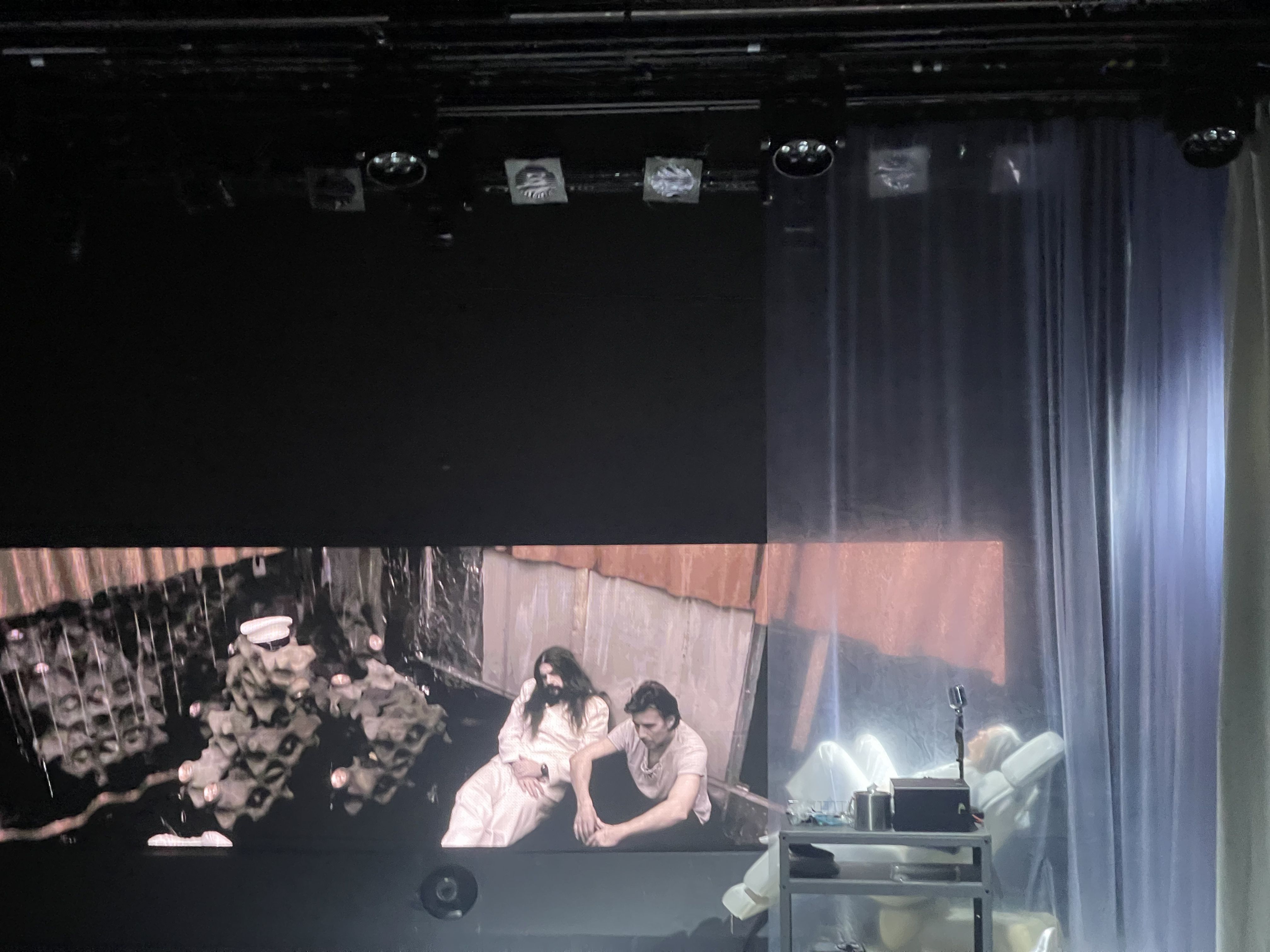 Bilde fra prøvene til Kallocain - en skuespiller ligger i en stol foran en skjerm hvor man kan se på menn som sitter lent mot en vegg