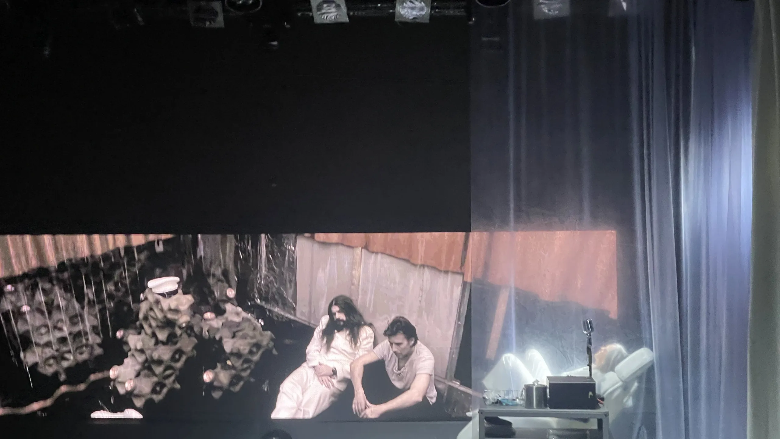 Bilde fra prøvene til Kallocain - en skuespiller ligger i en stol foran en skjerm hvor man kan se på menn som sitter lent mot en vegg