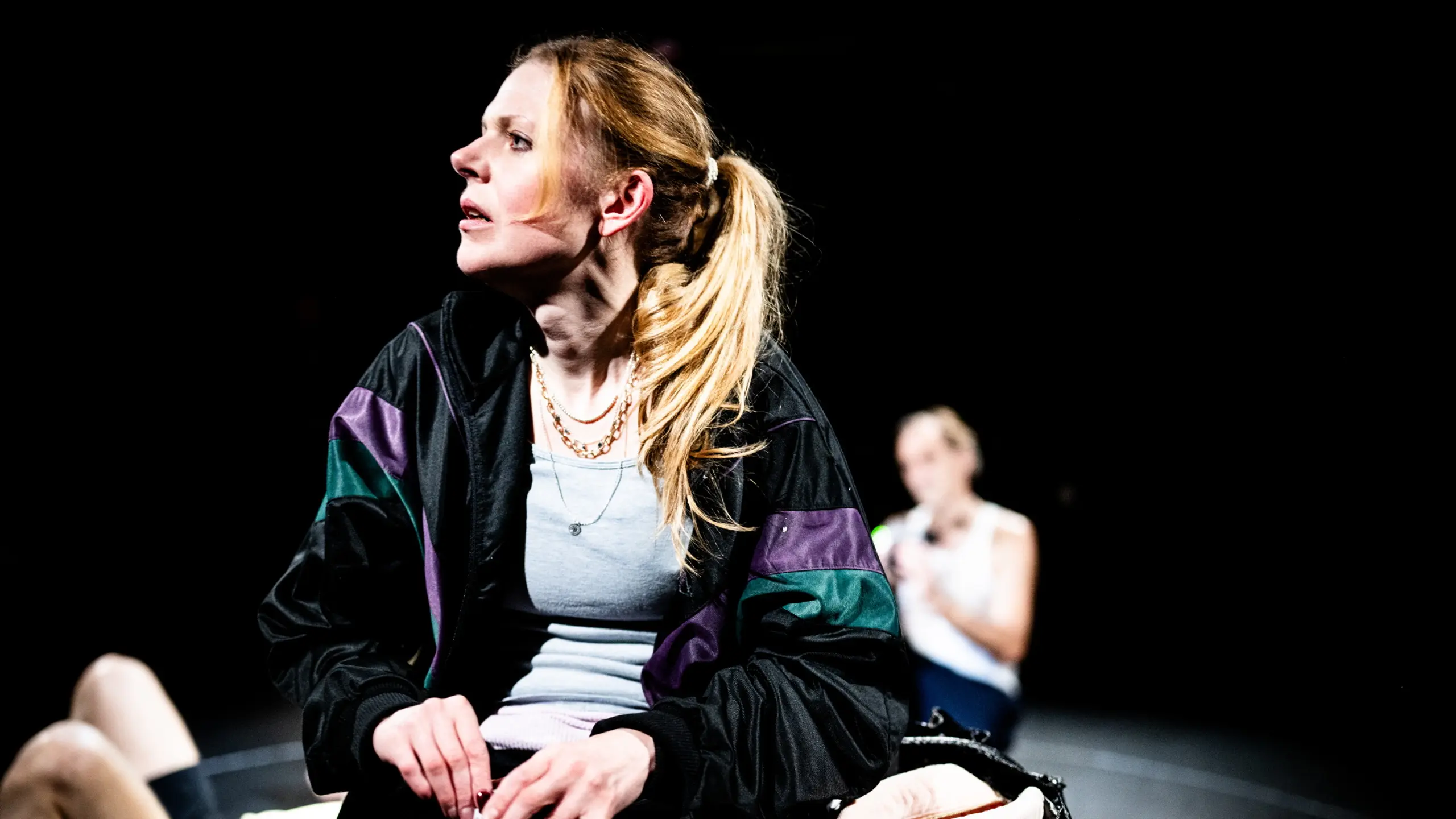 Kvinne i treningstøy sitter på scenekant og ser til siden, med ølboks og bag foran seg