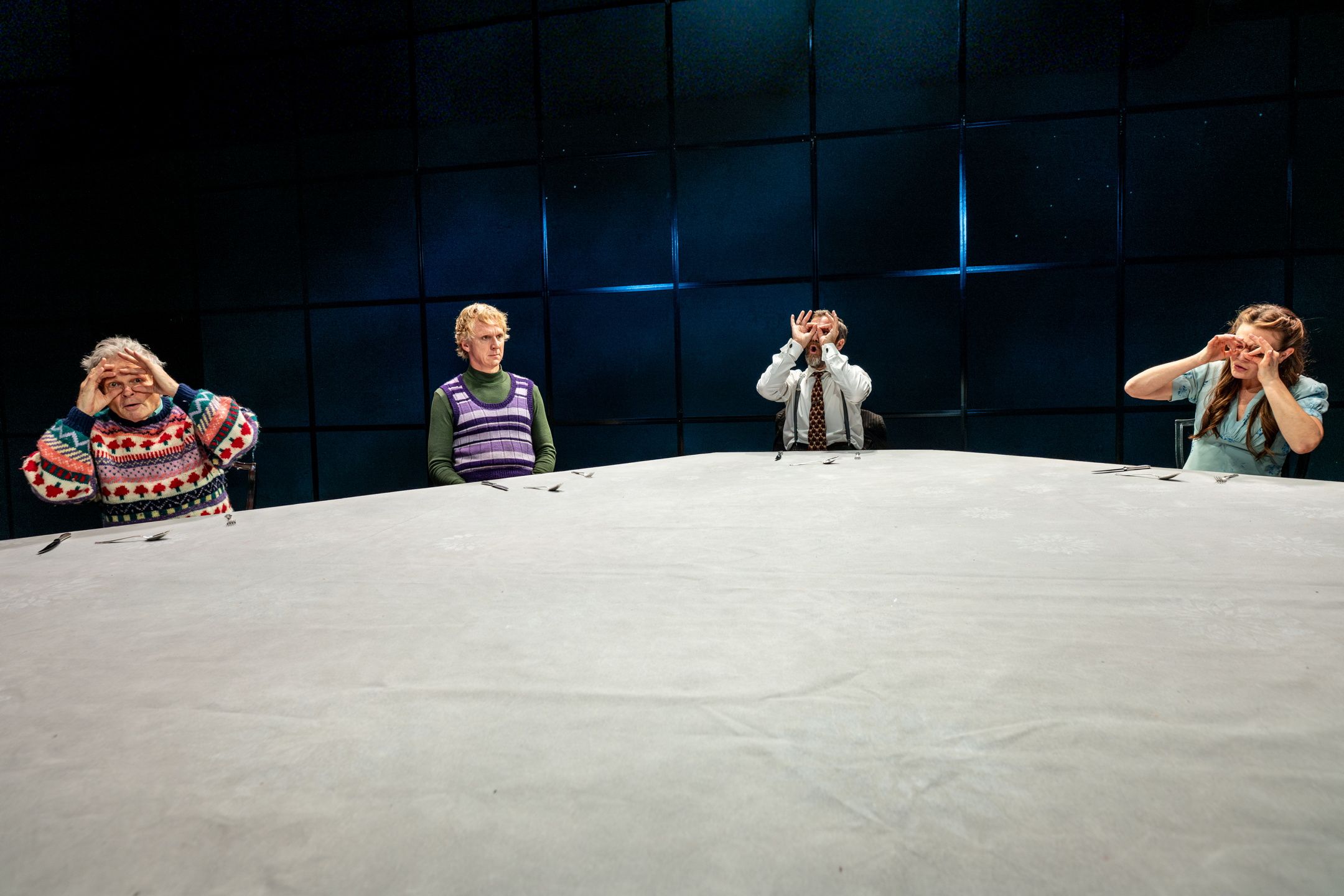 Fire personer rundt et stort bord; to holder hendene foran øynene som kikkert.