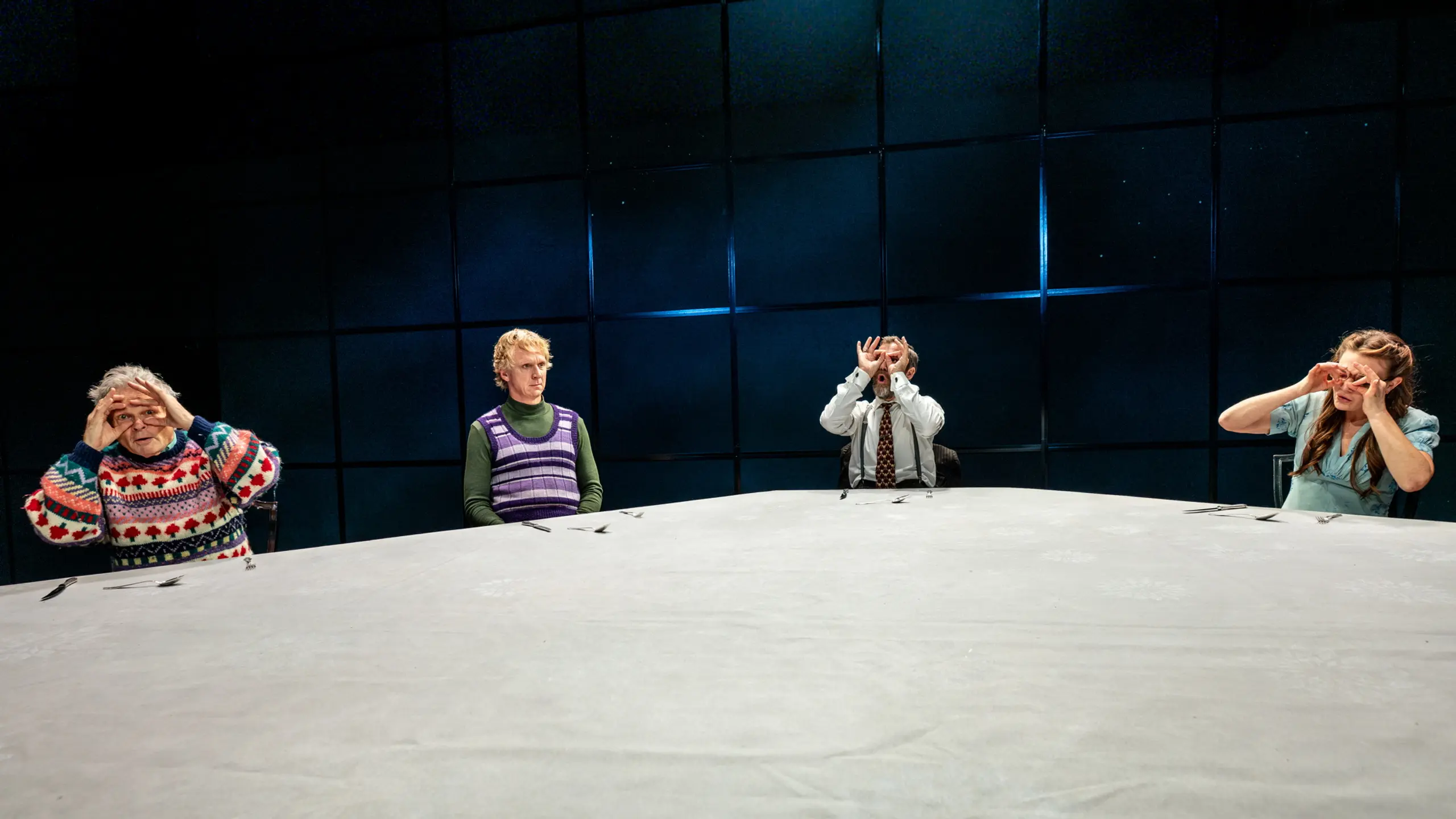 Fire personer rundt et stort bord; to holder hendene foran øynene som kikkert.