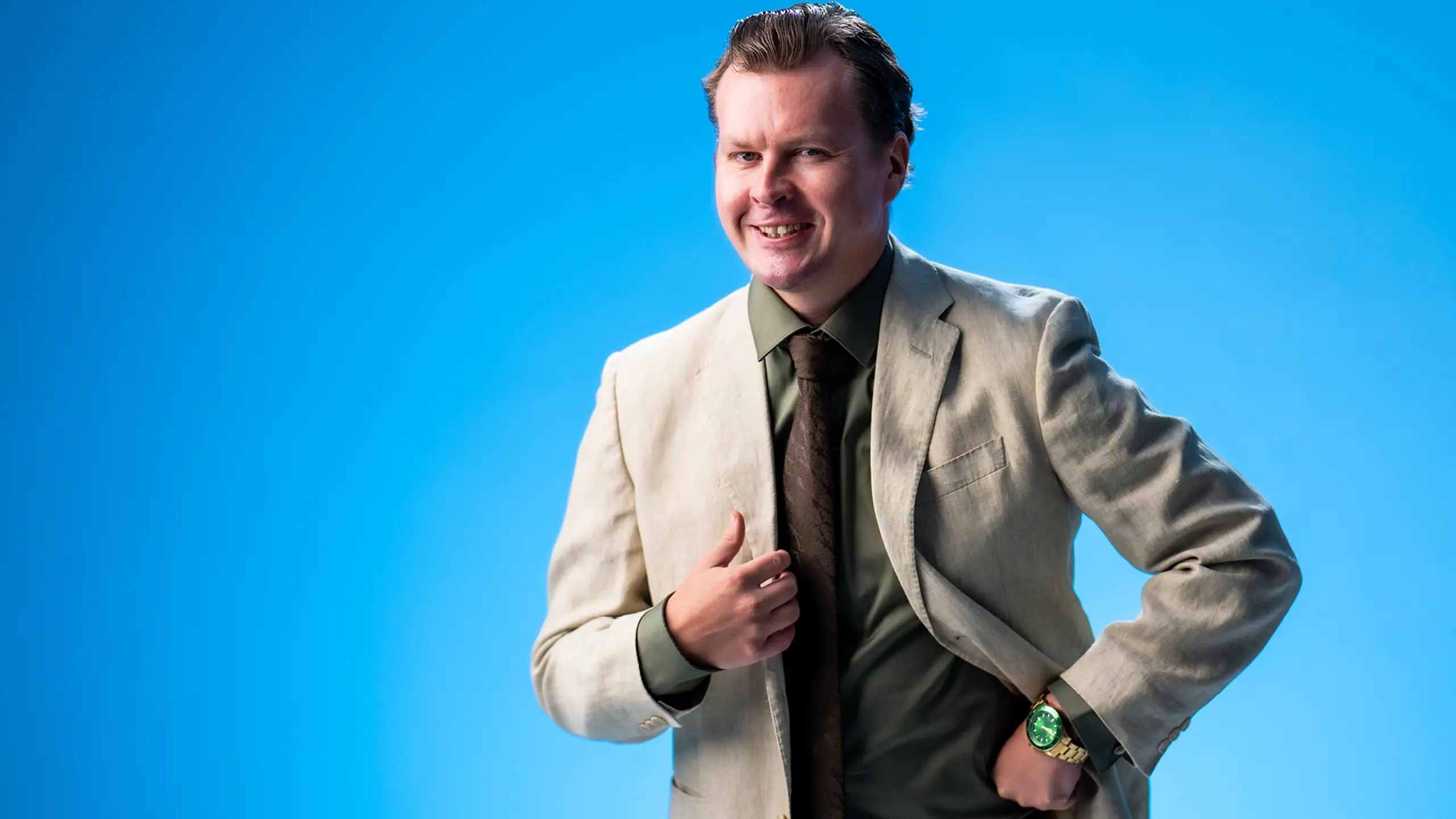 Smilende mann i dress mot blå bakgrunn.