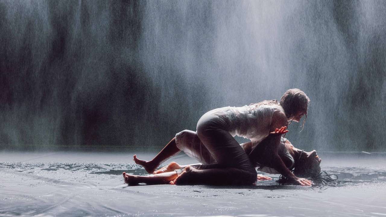 En kvinne ligger oppå en annen på mørk scene mens det duskregner