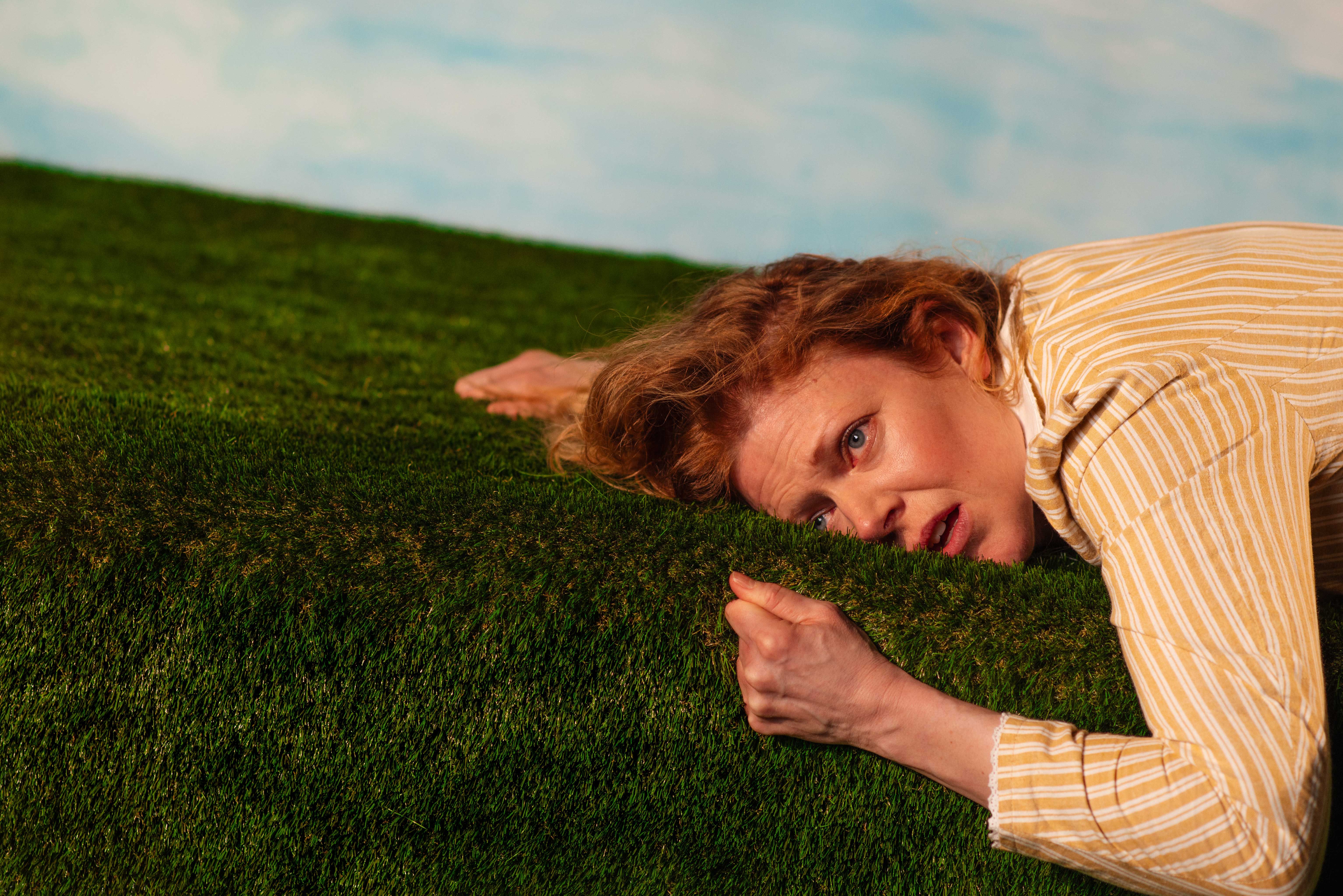 Kvinne som klamrer seg til kunstgress mot blå bakgrunn