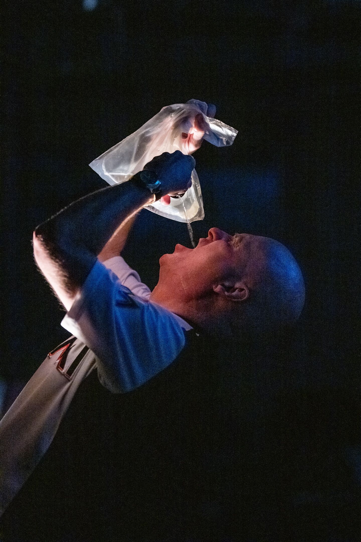 Mann i T-skjorte heller væske i munnen fra en gjennomsiktig plastpose