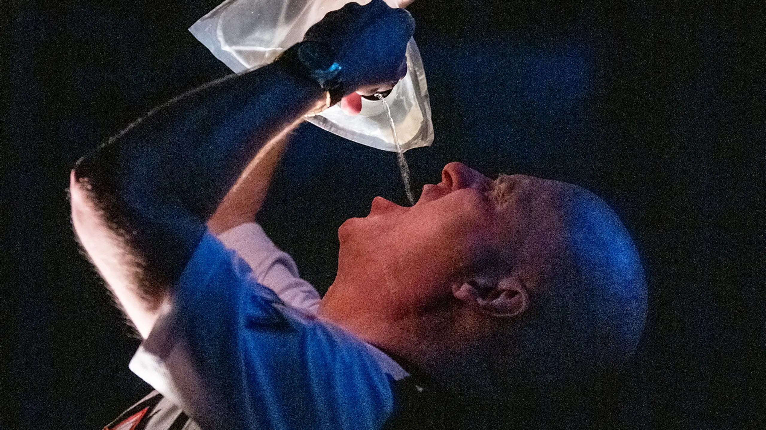 Mann i T-skjorte heller væske i munnen fra en gjennomsiktig plastpose