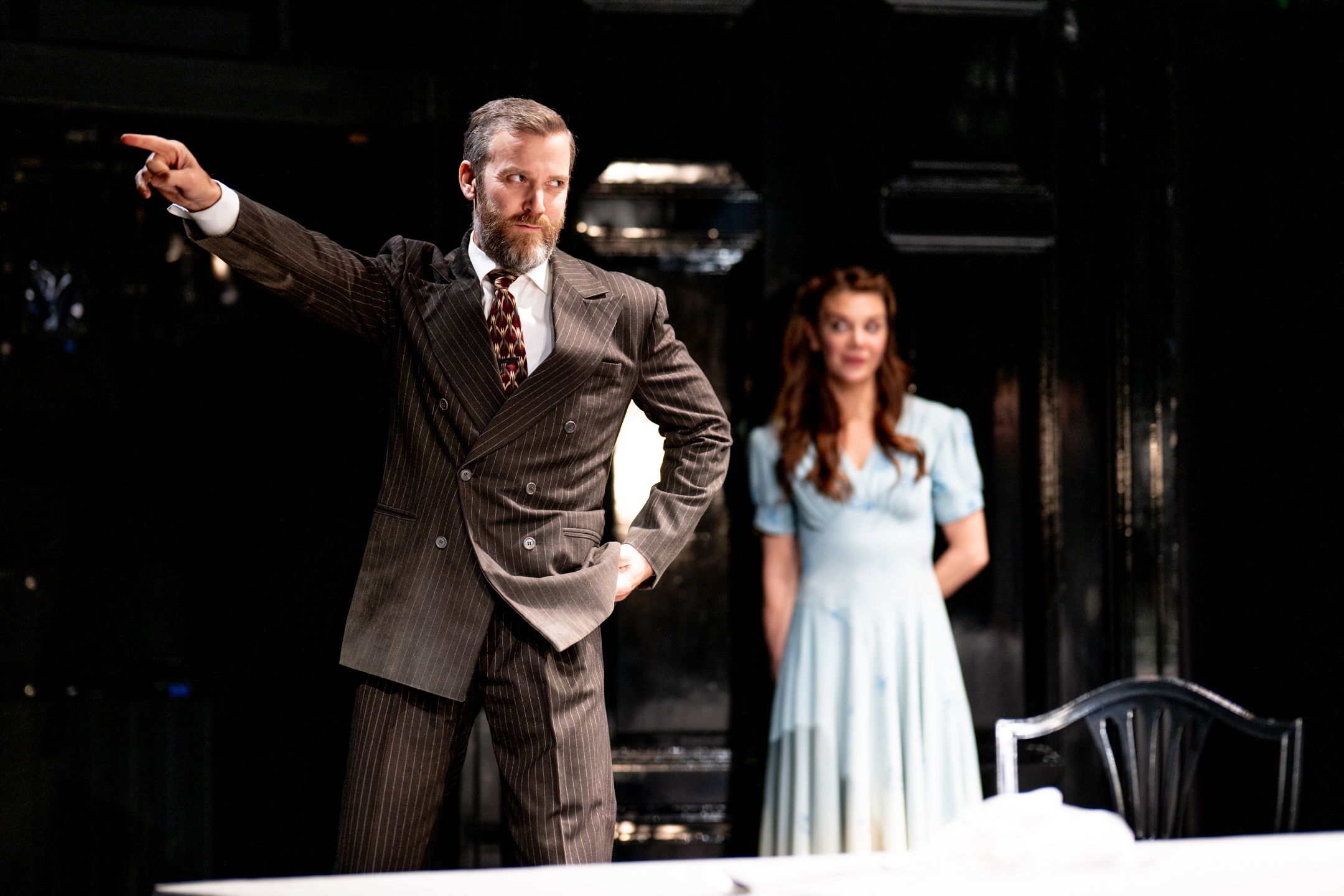 Mann i brun dress som peker. Kvinne i blå kjole i bakgrunnen