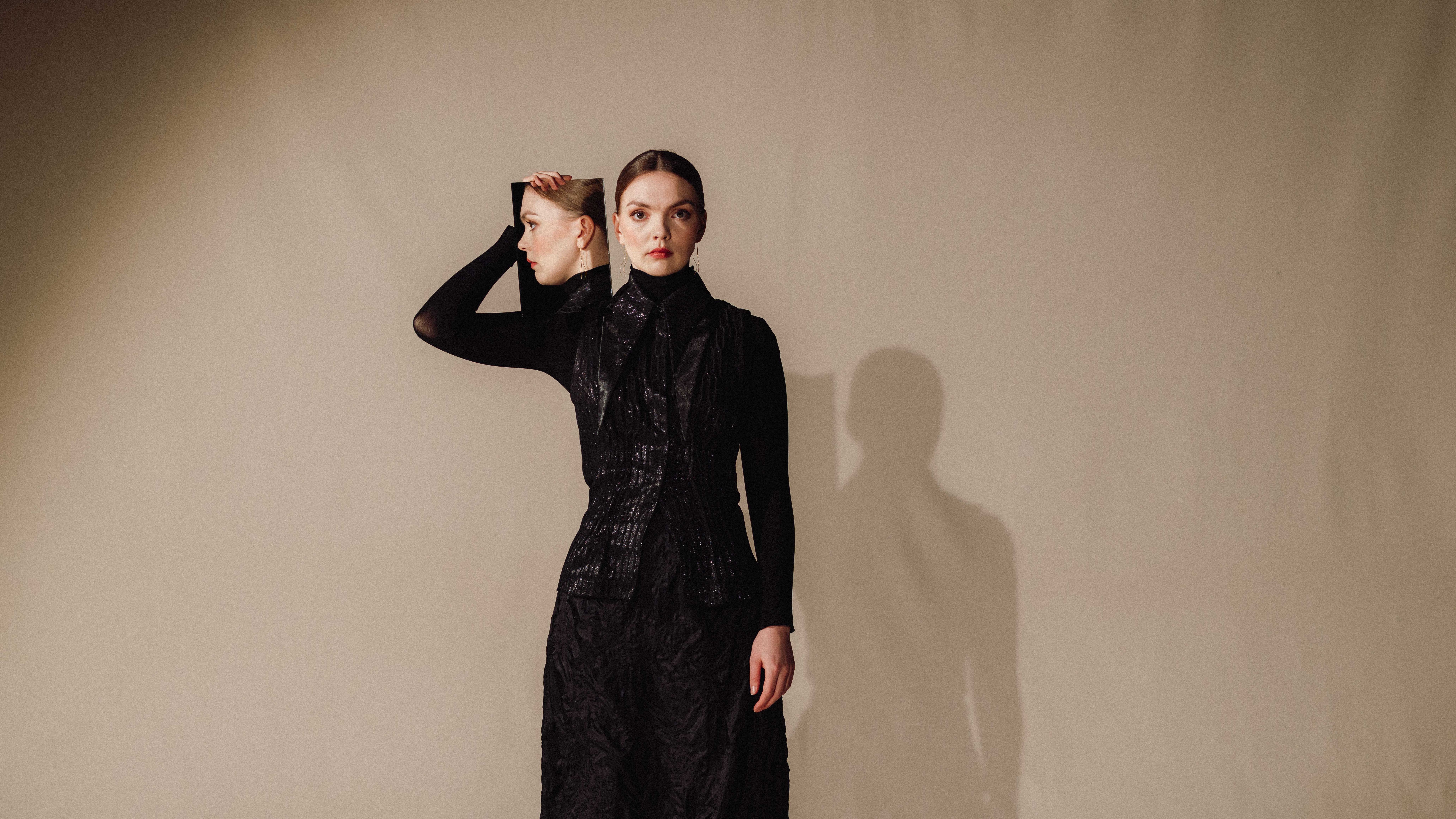 Kvinne i svart holder opp et speil ved siden av fjeset, så vi ser profilen hennes i det