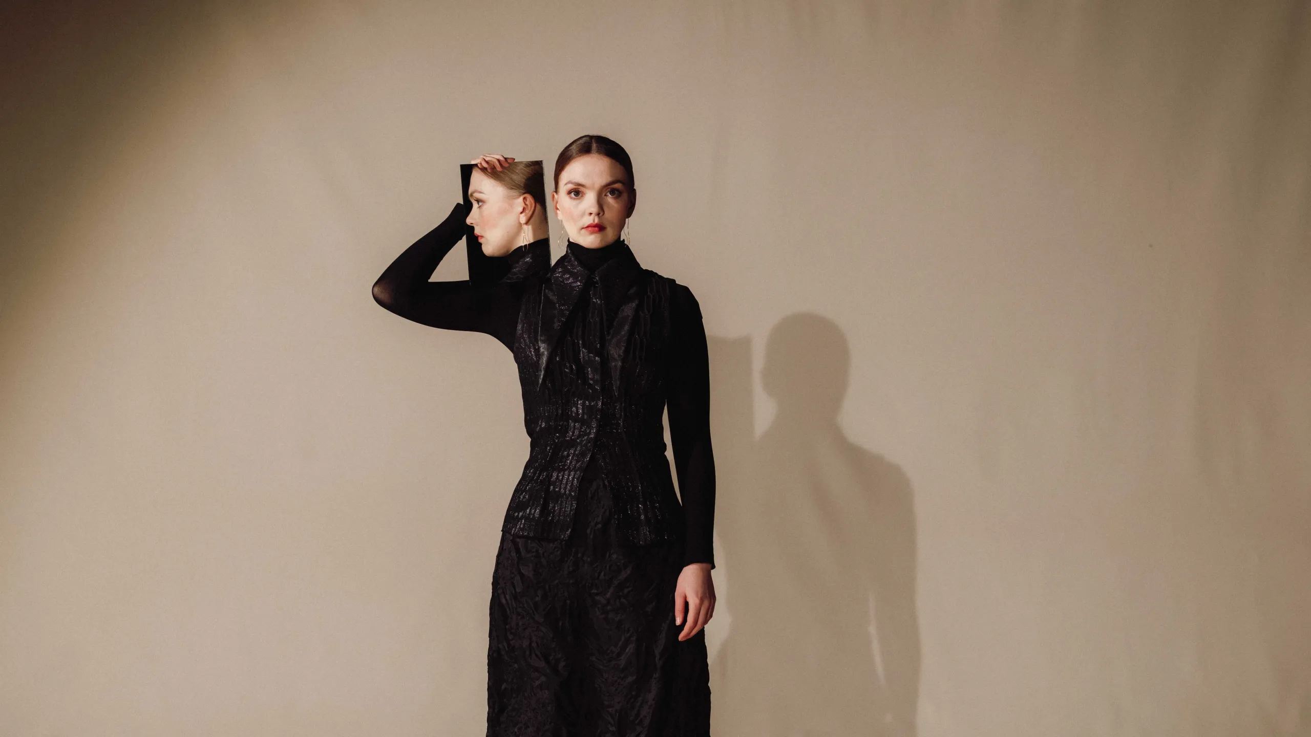 Kvinne i svart holder opp et speil ved siden av fjeset, så vi ser profilen hennes i det