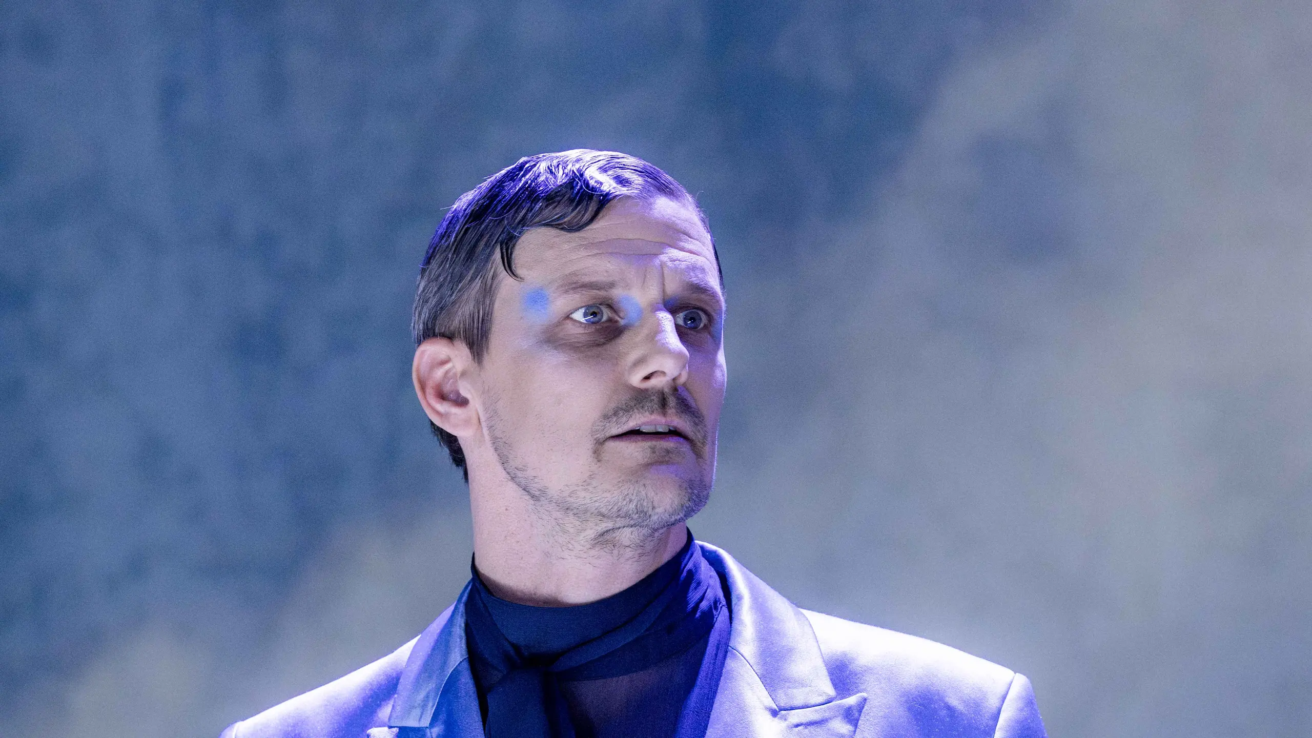 Person i lys blå dress holder en liten veske med stor sløyfe, ser opp mot siden i scenelys