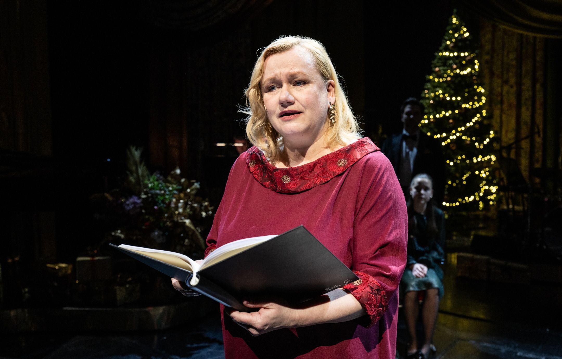 Kvinne på julepyntet scene som leser fra en bok