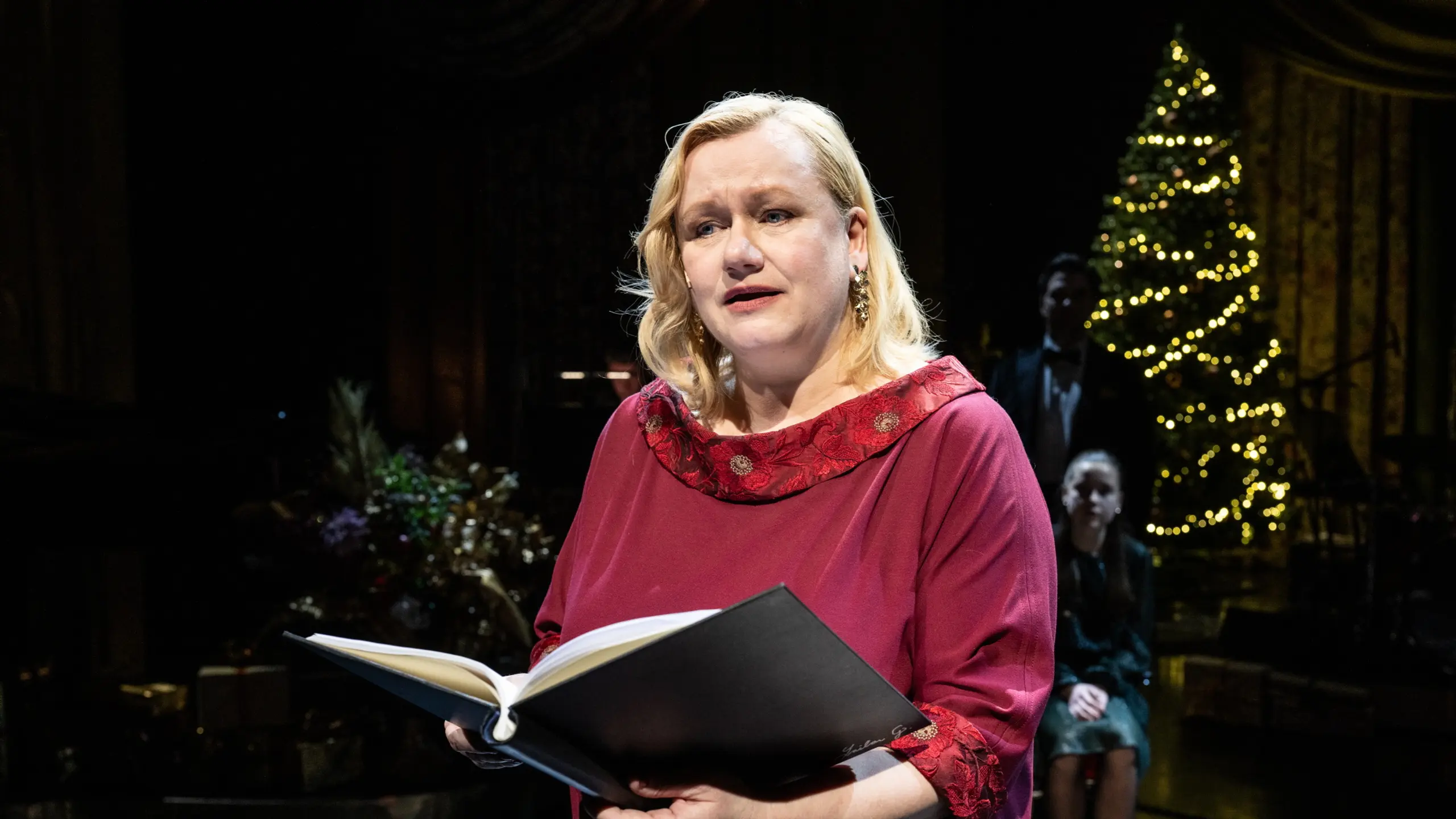 Kvinne på julepyntet scene som leser fra en bok