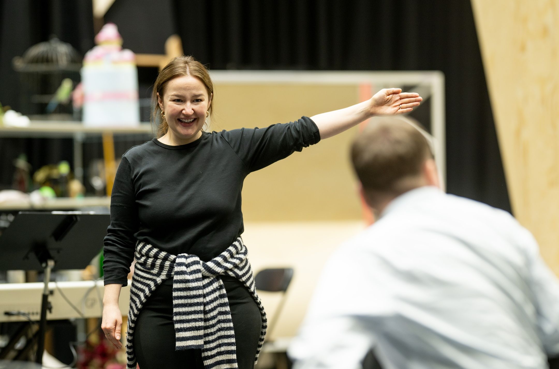 En kvinne i svart genser smiler og gestikulerer mot en mann i lyseblå skjorte med ryggen til kamera.