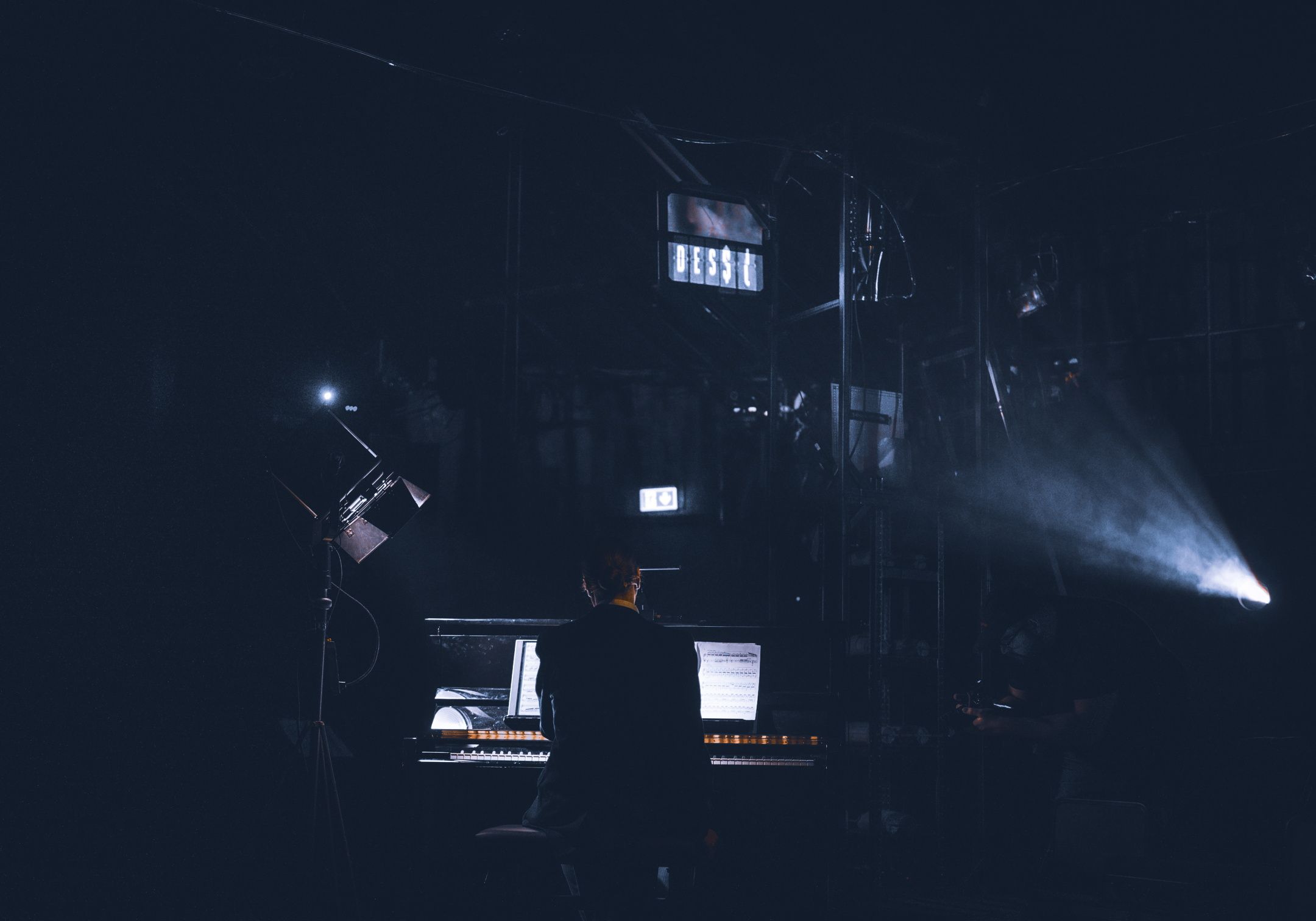 Mann sitter ved piano i scenelys med ryggen til kamera