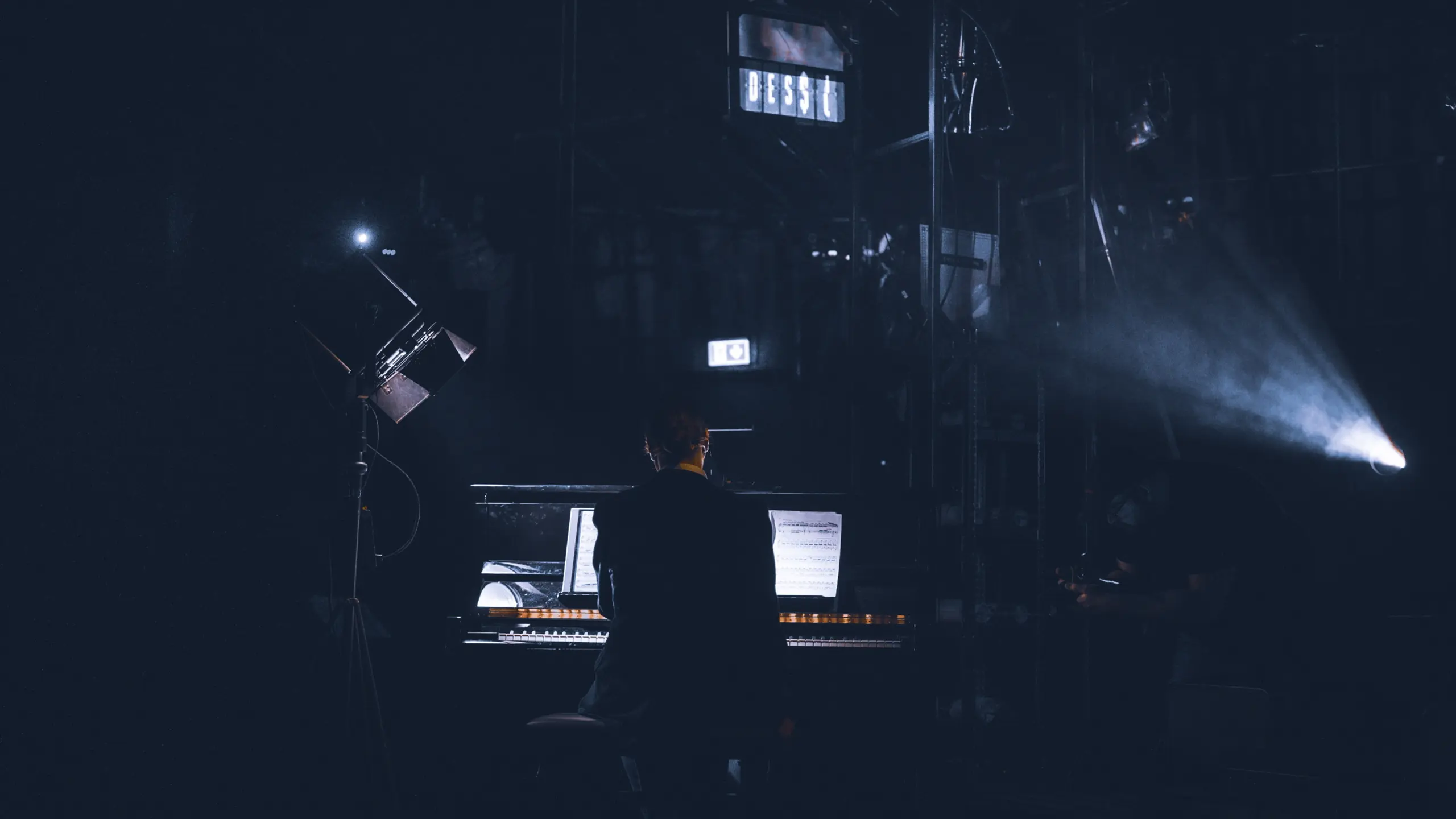 Mann sitter ved piano i scenelys med ryggen til kamera