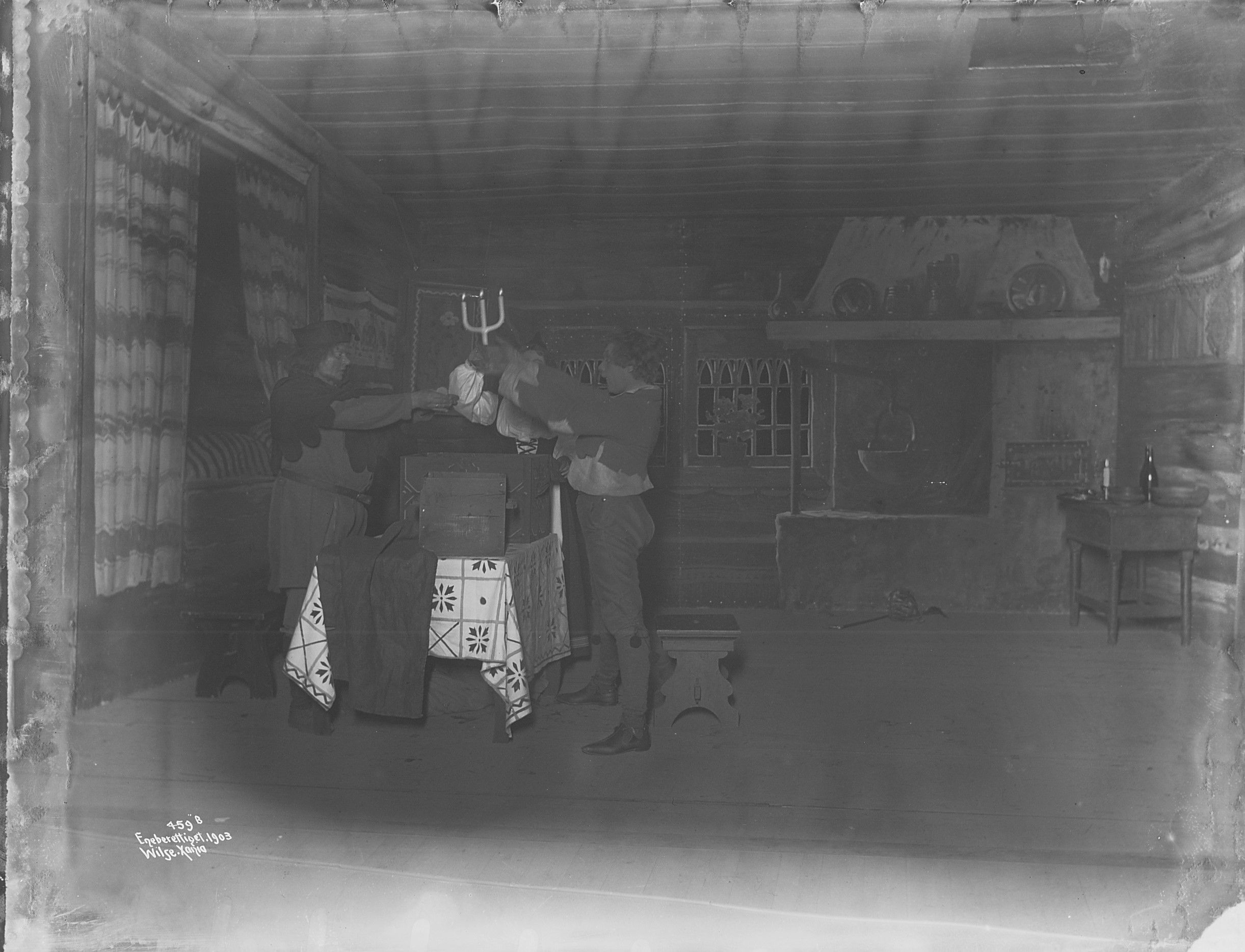 Gammelt svart-hvitt bilde av to personer i en gammeldags stue-scenografi