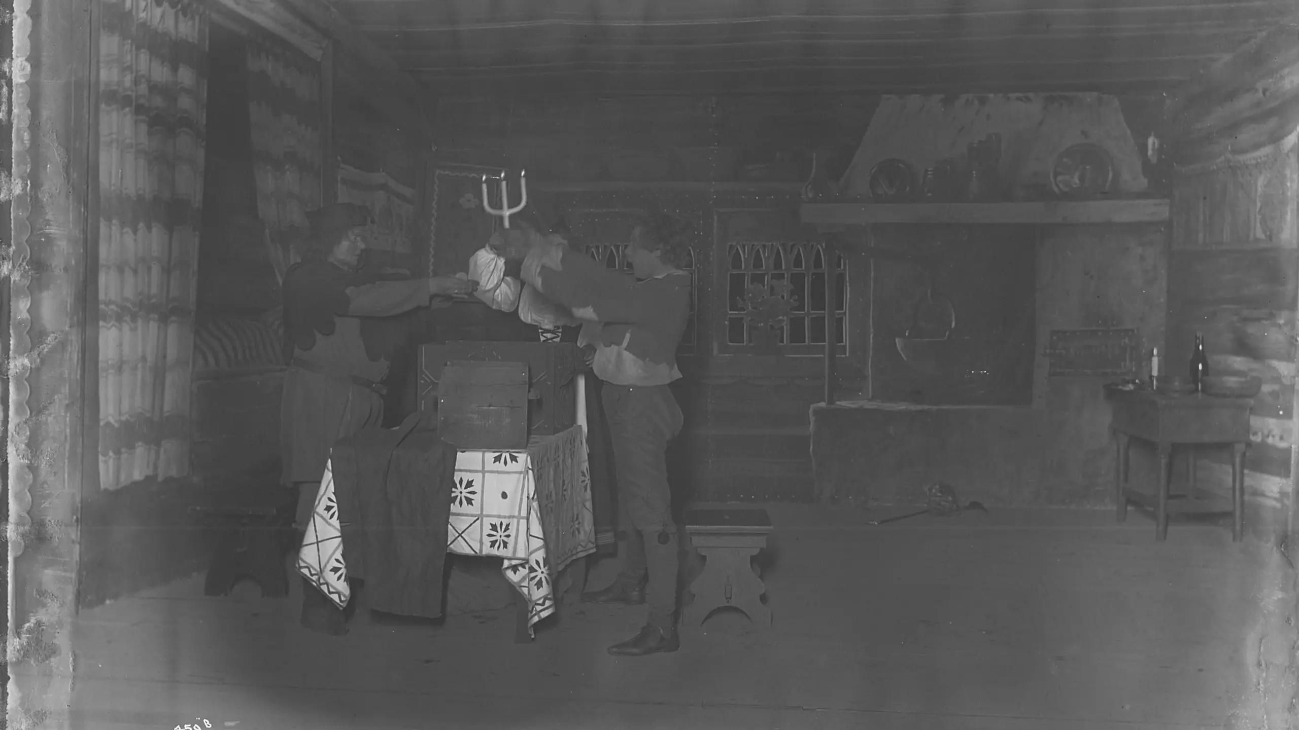 Gammelt svart-hvitt bilde av to personer i en gammeldags stue-scenografi