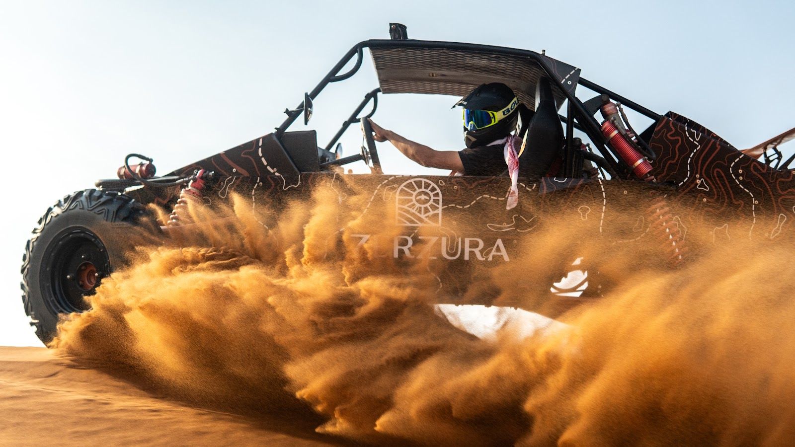 A helmeted Zerzura dune buggy driver behind a roll cage with a mounted fire extinguisher