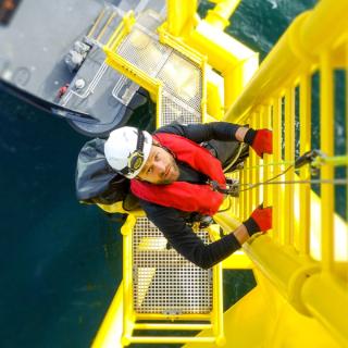 Worker climbing yellow ladder on monopile