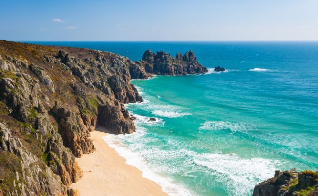 A beautiful, secluded sandy beach with turquoise waters surrounded by large dark cliffs