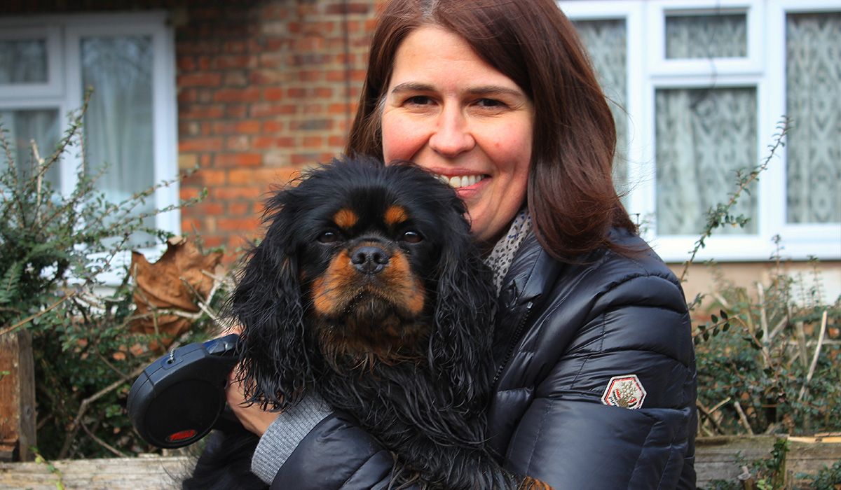 A small, long-haired, black and tan dog is in the arms of a smiling woman