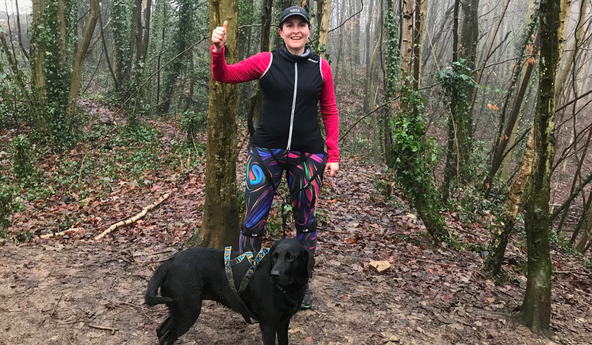 Runner, Nicola and her borrowed dog, Lola, a black Labrador Retriever, take a break in the woods on a club run.